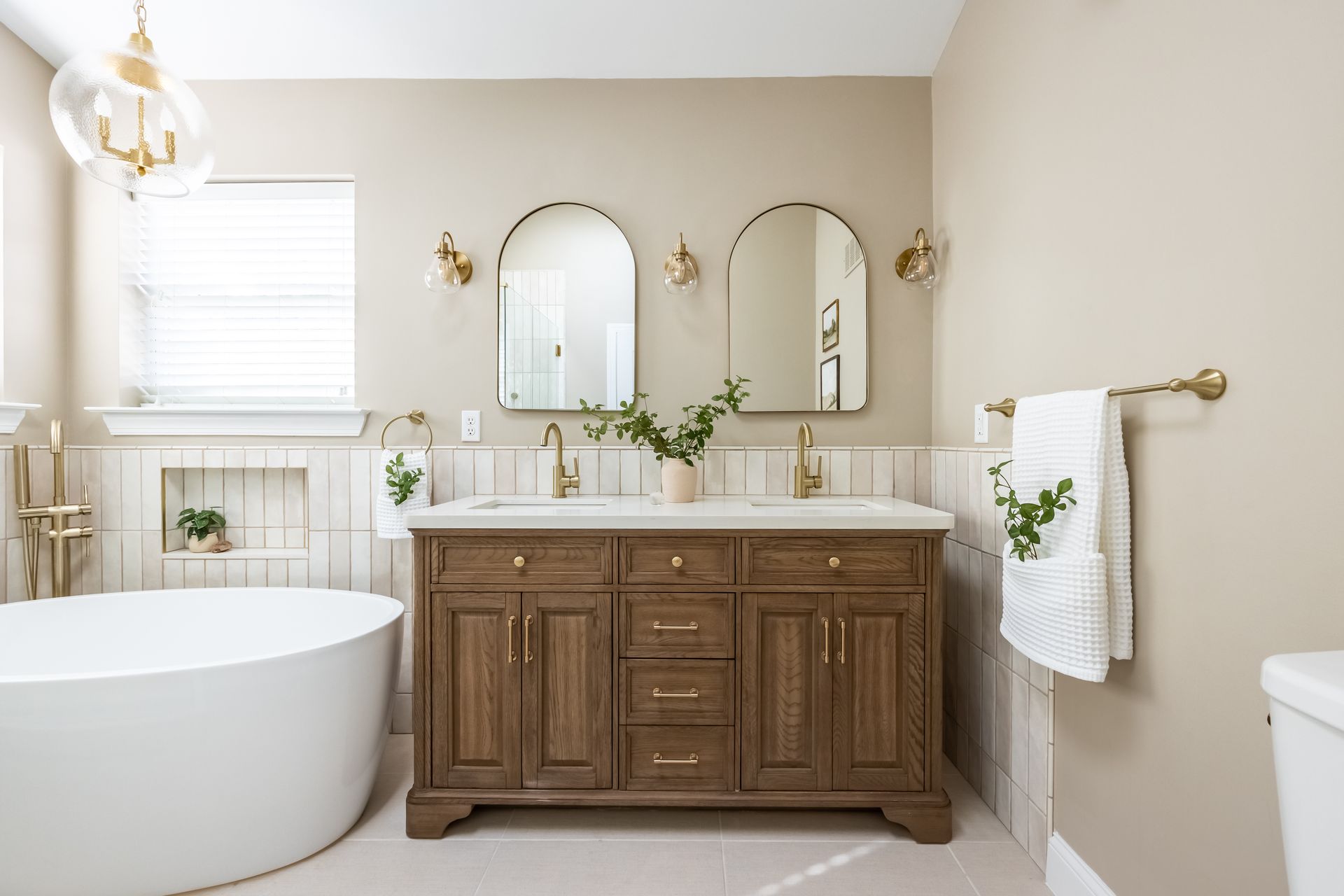 Bathroom with a wooden vanity, oval mirrors, and a freestanding tub.