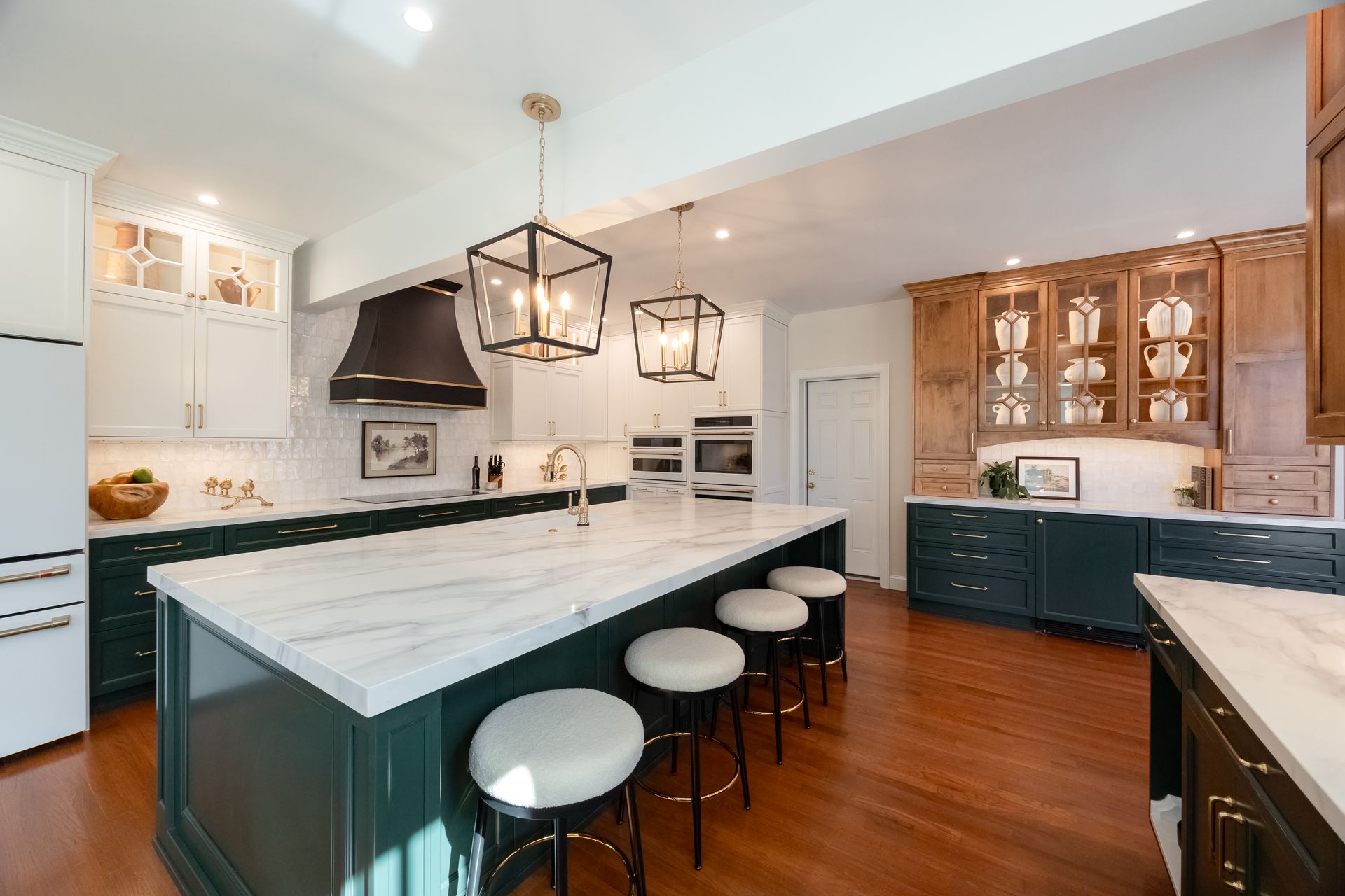 Spacious kitchen with a large island, green cabinets, marble countertops, and pendant lights.