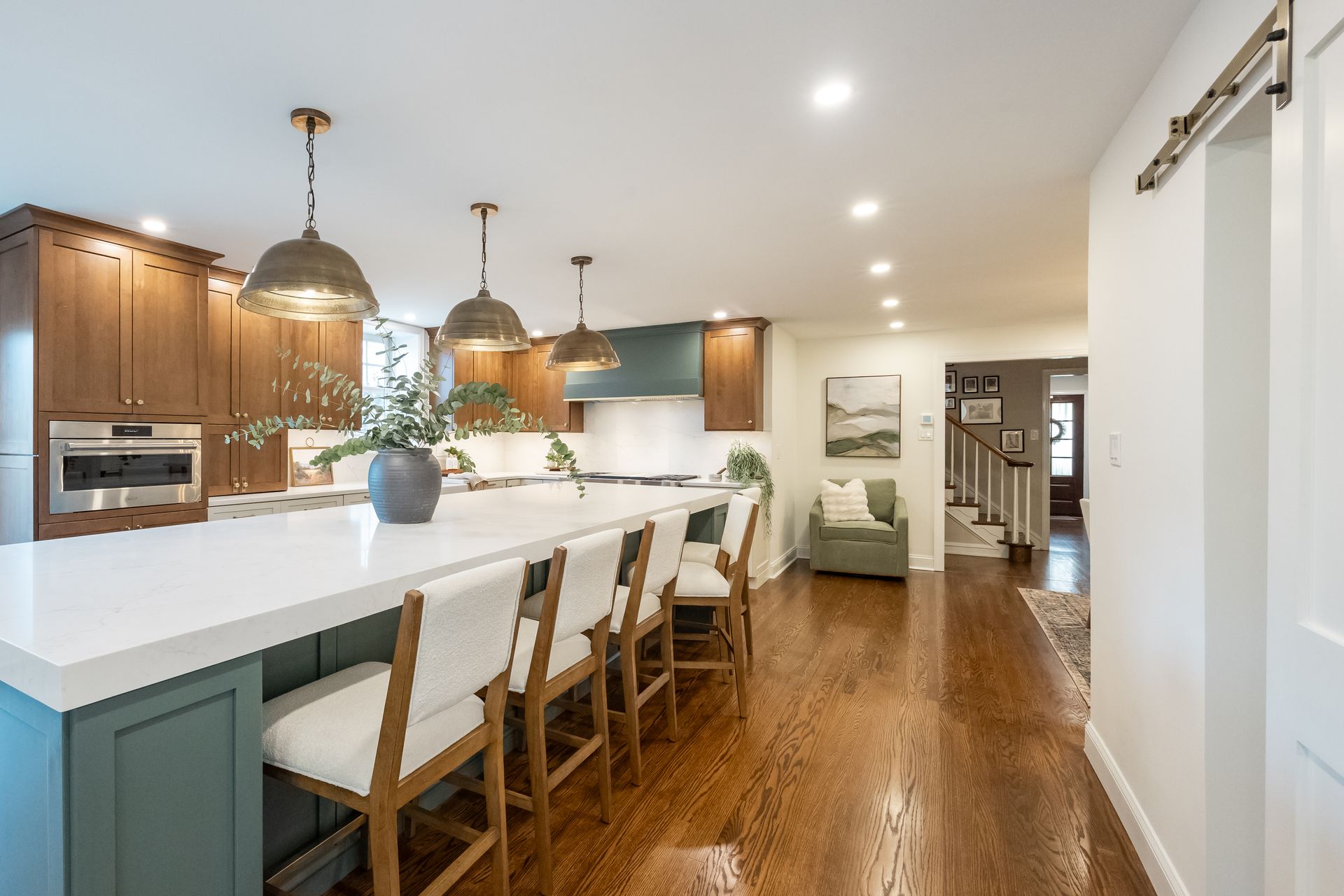 Kitchen with a white island, wooden cabinets, and teal accents; pendant lights hang above the island.