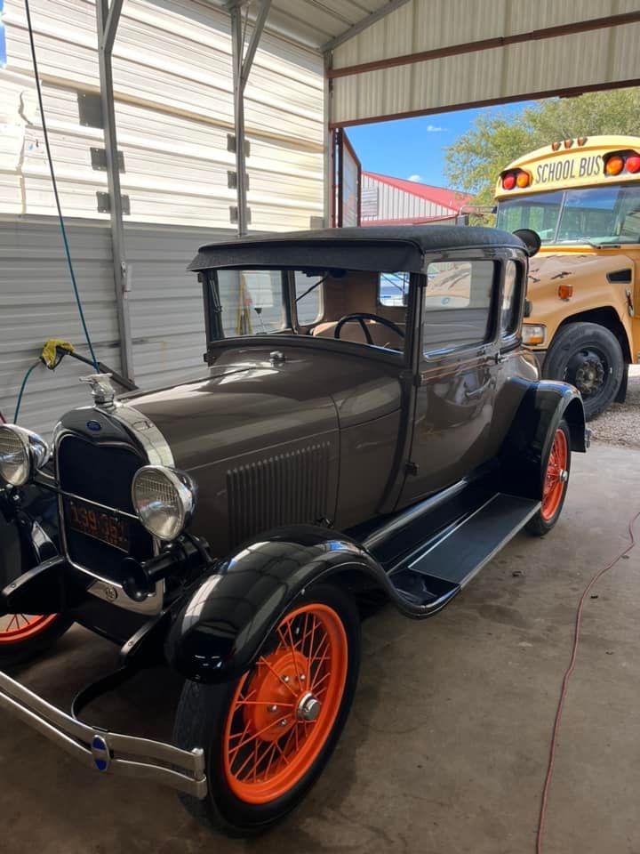 An old car is parked in a garage next to a school bus.