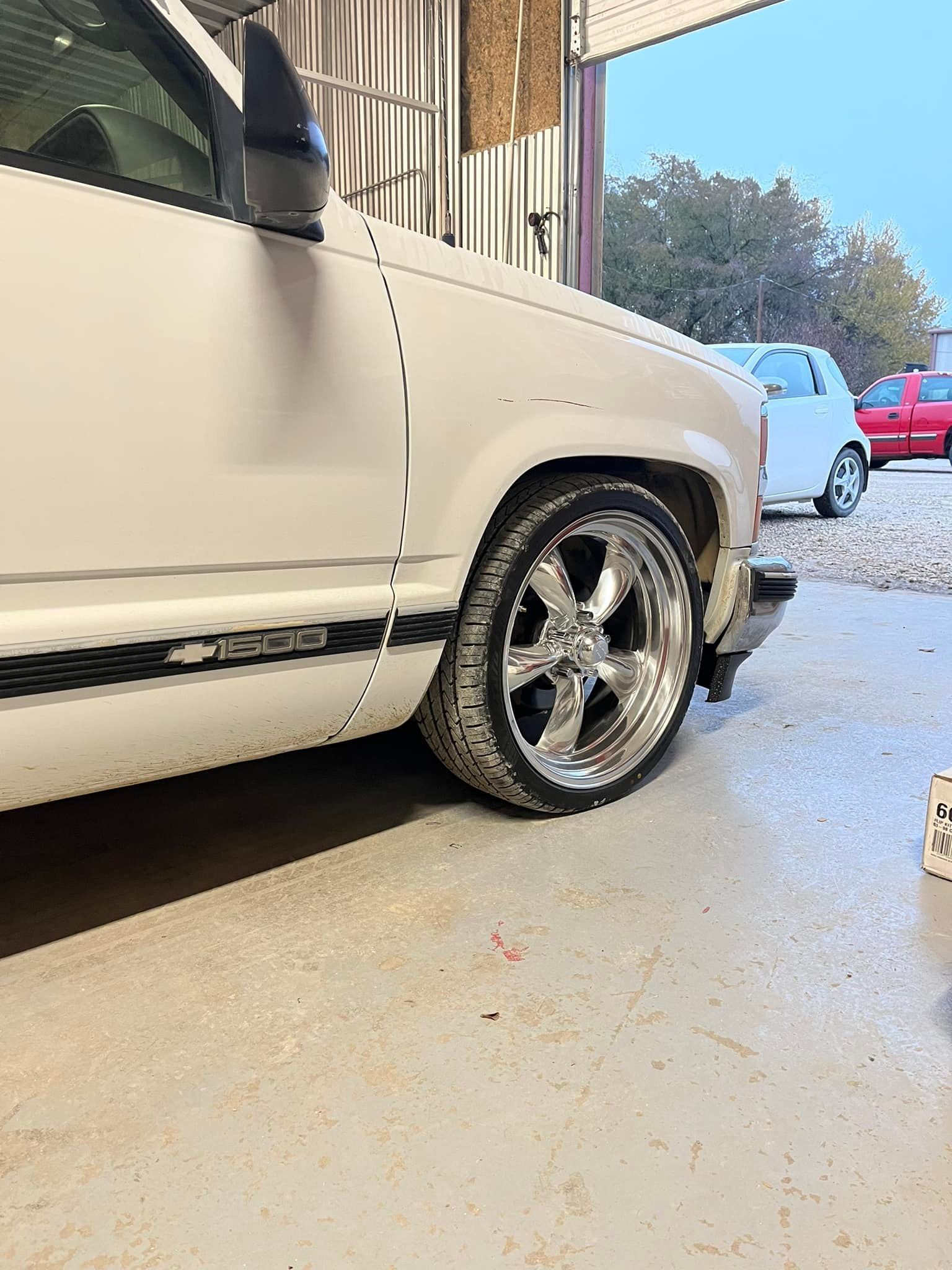 A white truck with chrome wheels is parked in a garage.