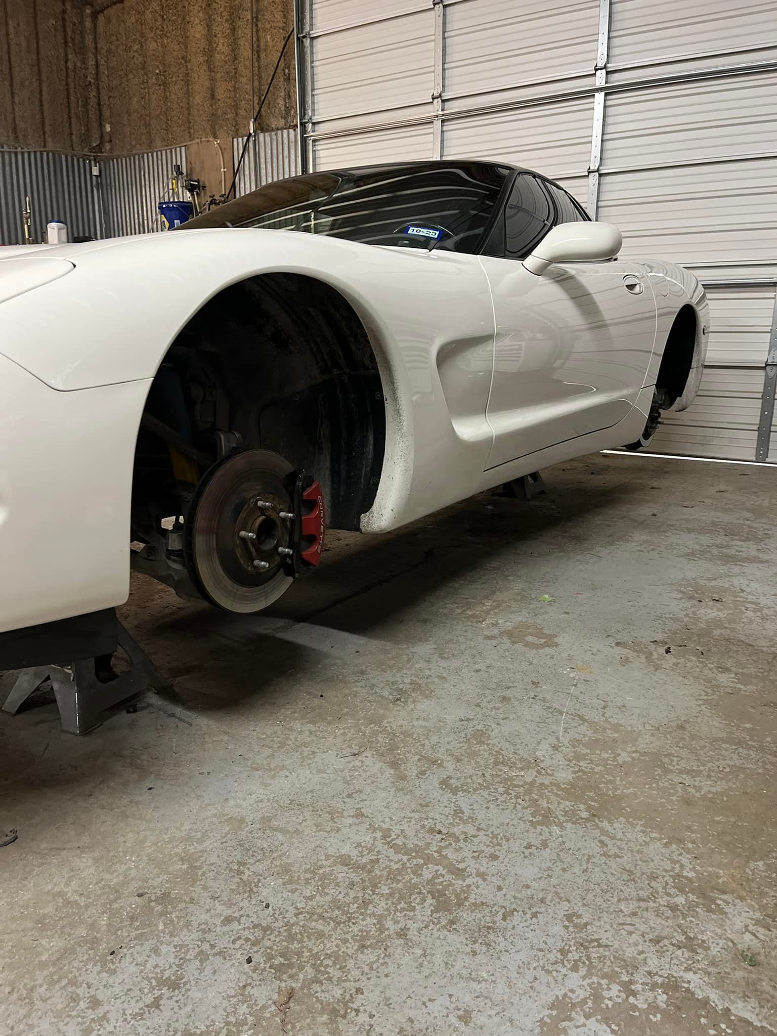 A white sports car is parked in a garage next to a garage door.