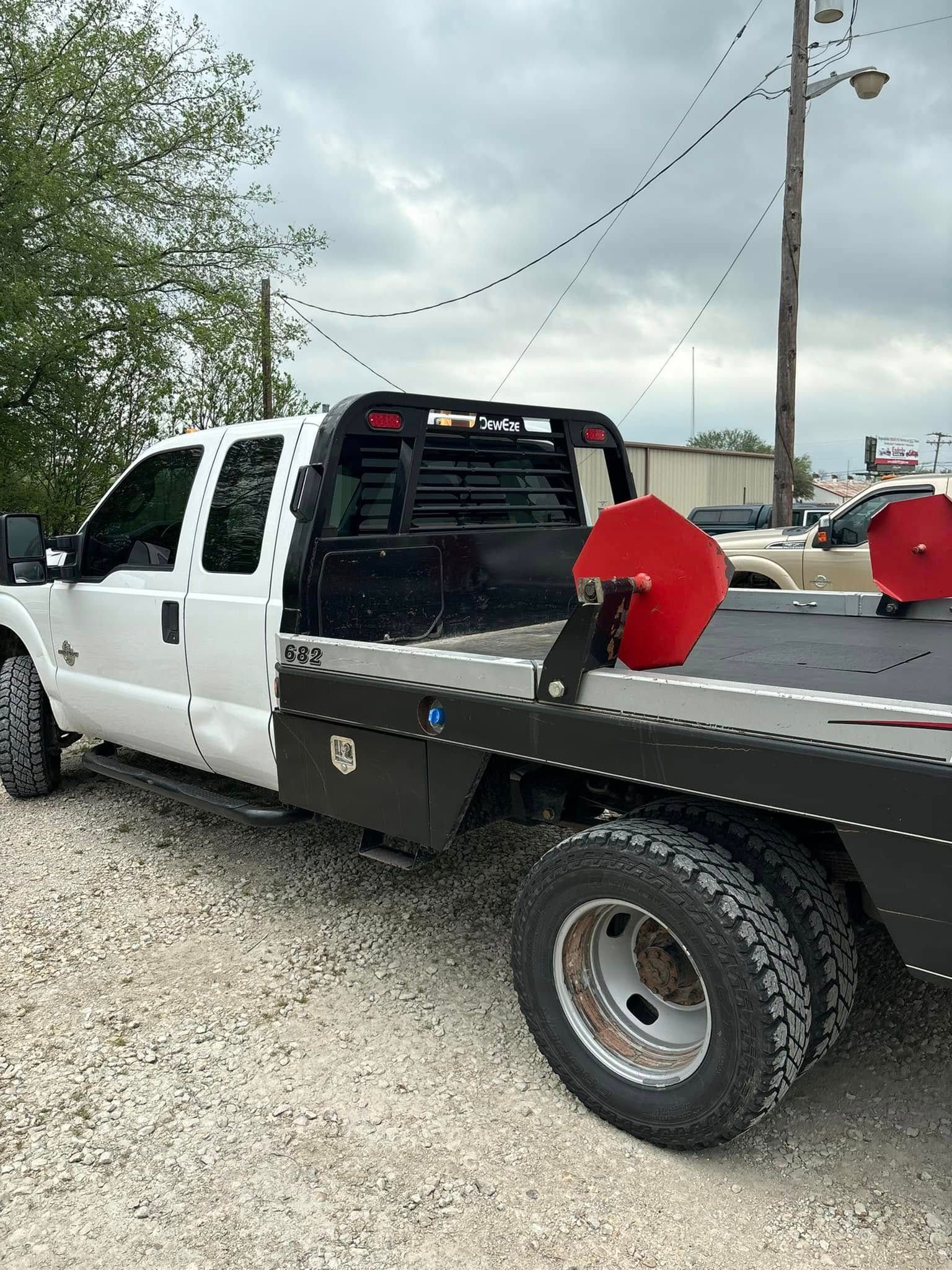 A white tow truck with a flat bed is parked in a gravel lot.