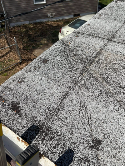 A high-angle view looking down at a weathered, gray flat roof with patched seams and dark spots.