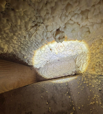 Spray foam insulation applied to a wooden structural joint, illuminated by a bright circular light.