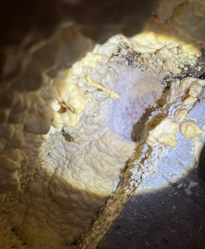 A close-up view of beige, hardened spray foam insulation filling a gap in a dark, textured building structure.
