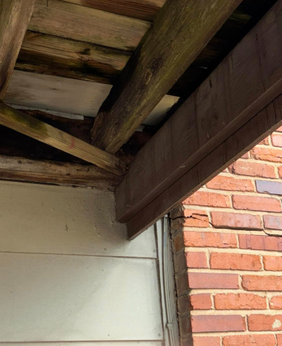 View from below of a deck structure showing severe wood rot and decay at the connection to a brick and siding wall.