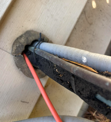 Close-up of utility lines, including a bright orange cable, entering a wall through an opening sealed with dark putty.