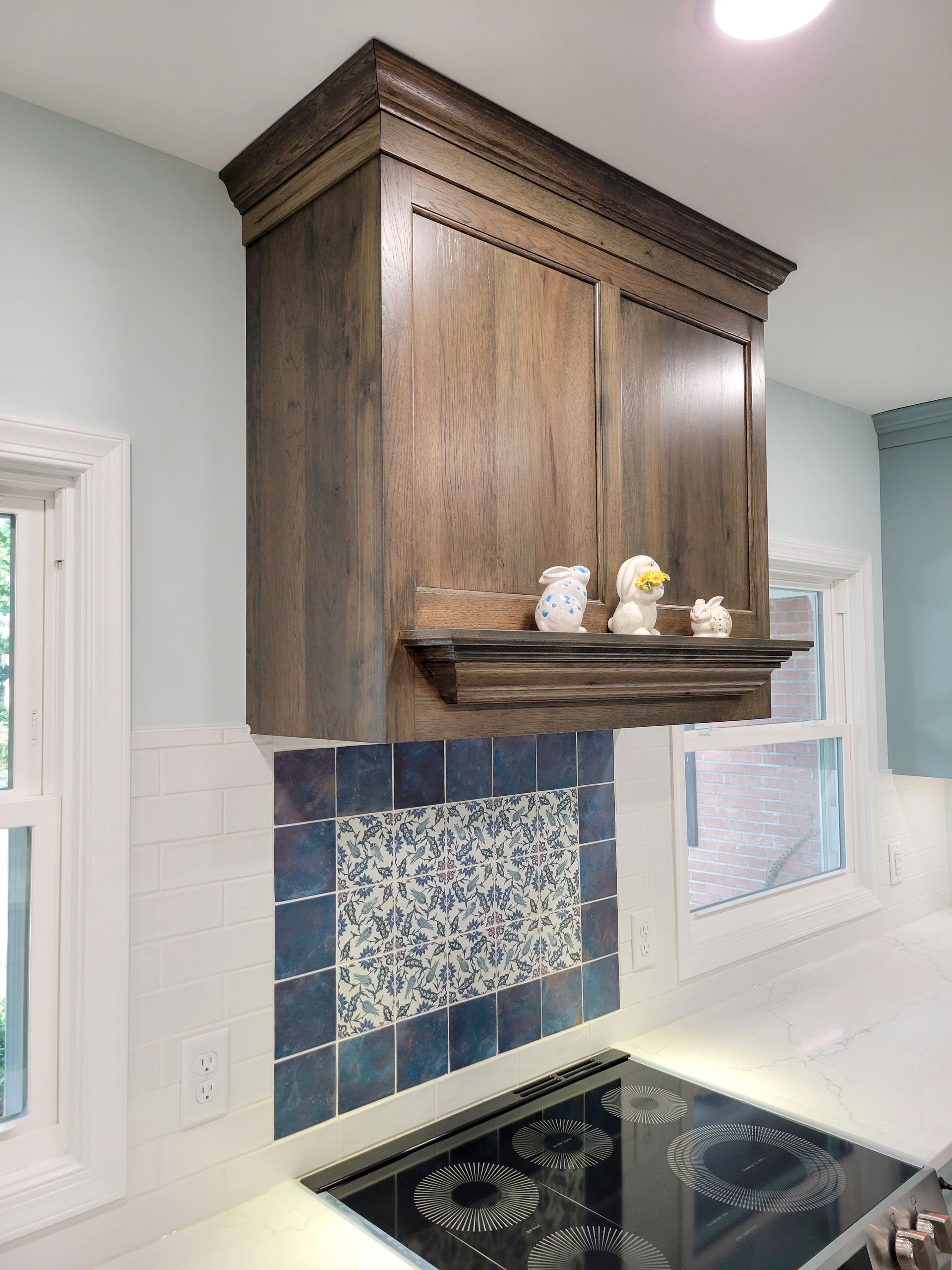 Custom kitchen hood with blue floral backsplash tile and Sherwin-Williams Interesting Aqua cabinets.