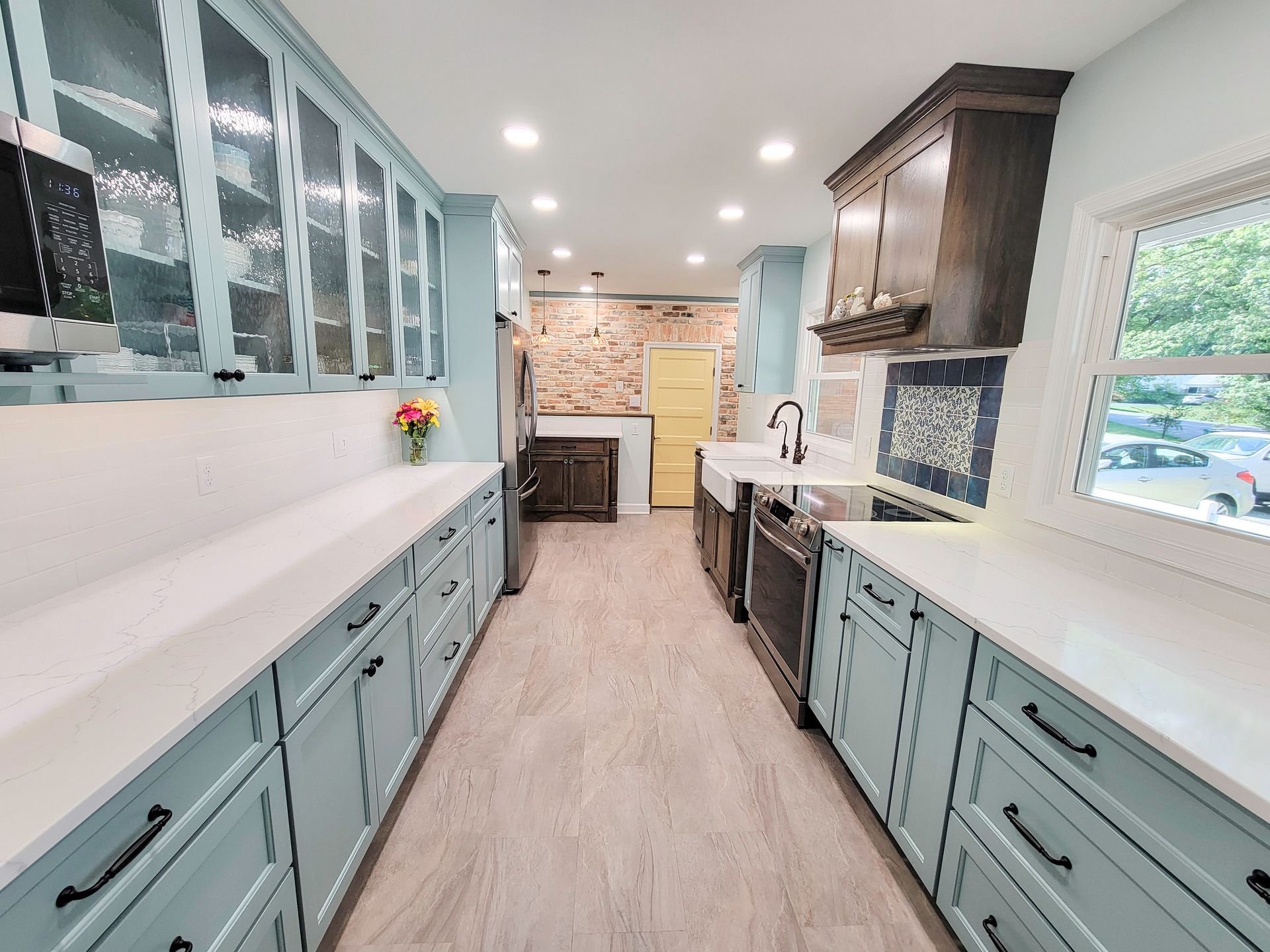 Open transitional kitchen design with aqua cabinetry, brick feature wall, and custom hood with wood accents.