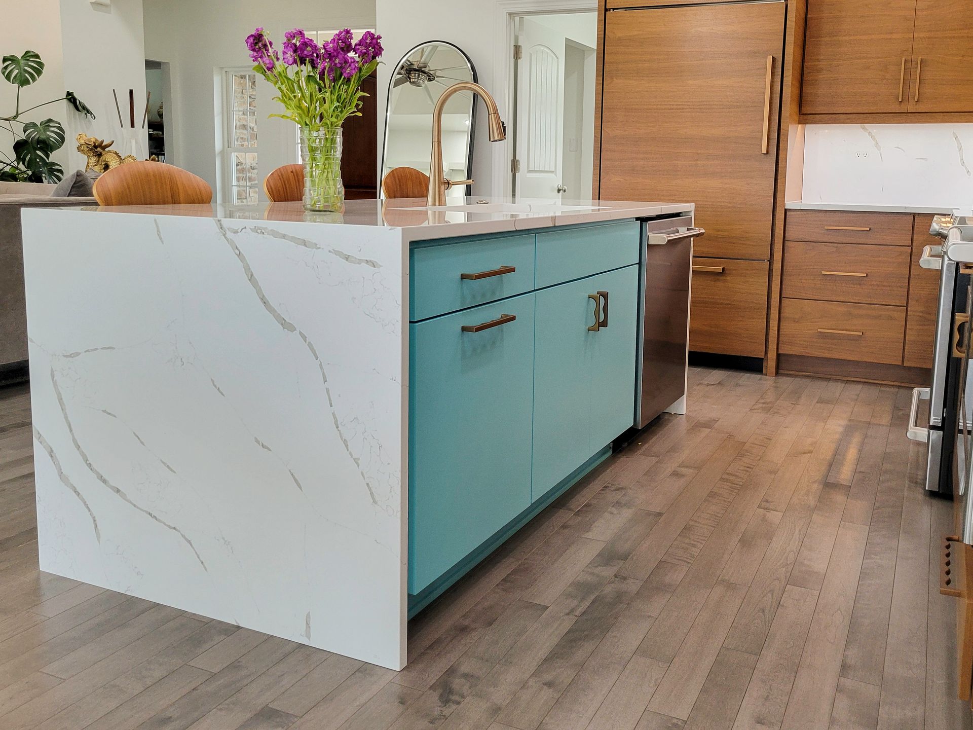 Modern kitchen with white marble island, teal cabinets, wooden floors, and flowers on the counter