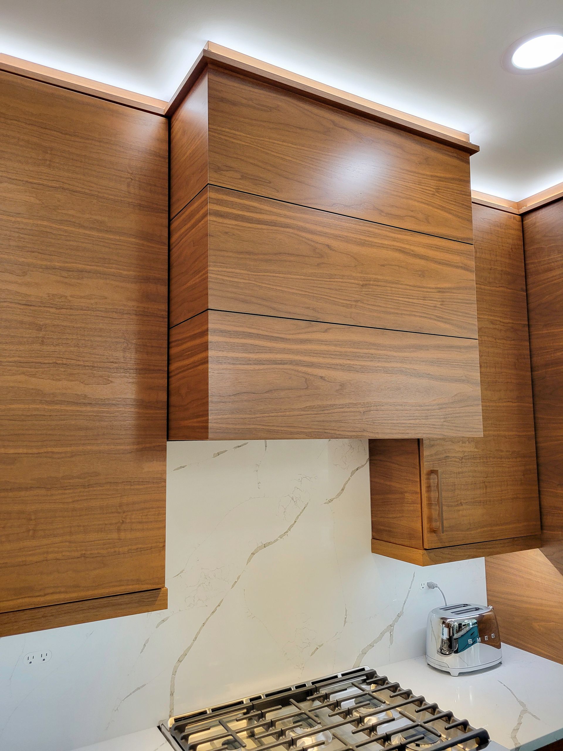Wooden kitchen cabinets above a stove and marble backsplash in a modern kitchen.