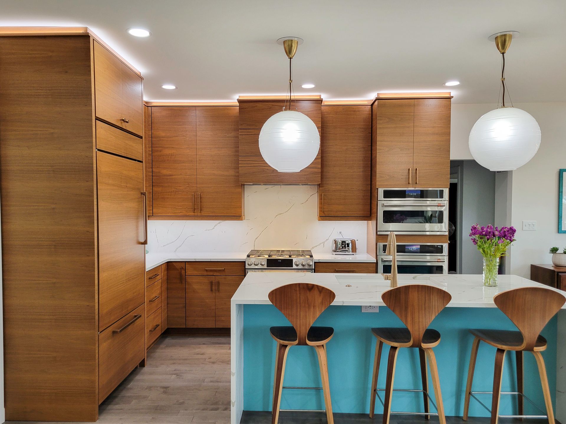 Modern kitchen with wood cabinets, teal island, and three bar stools under globe pendant lights