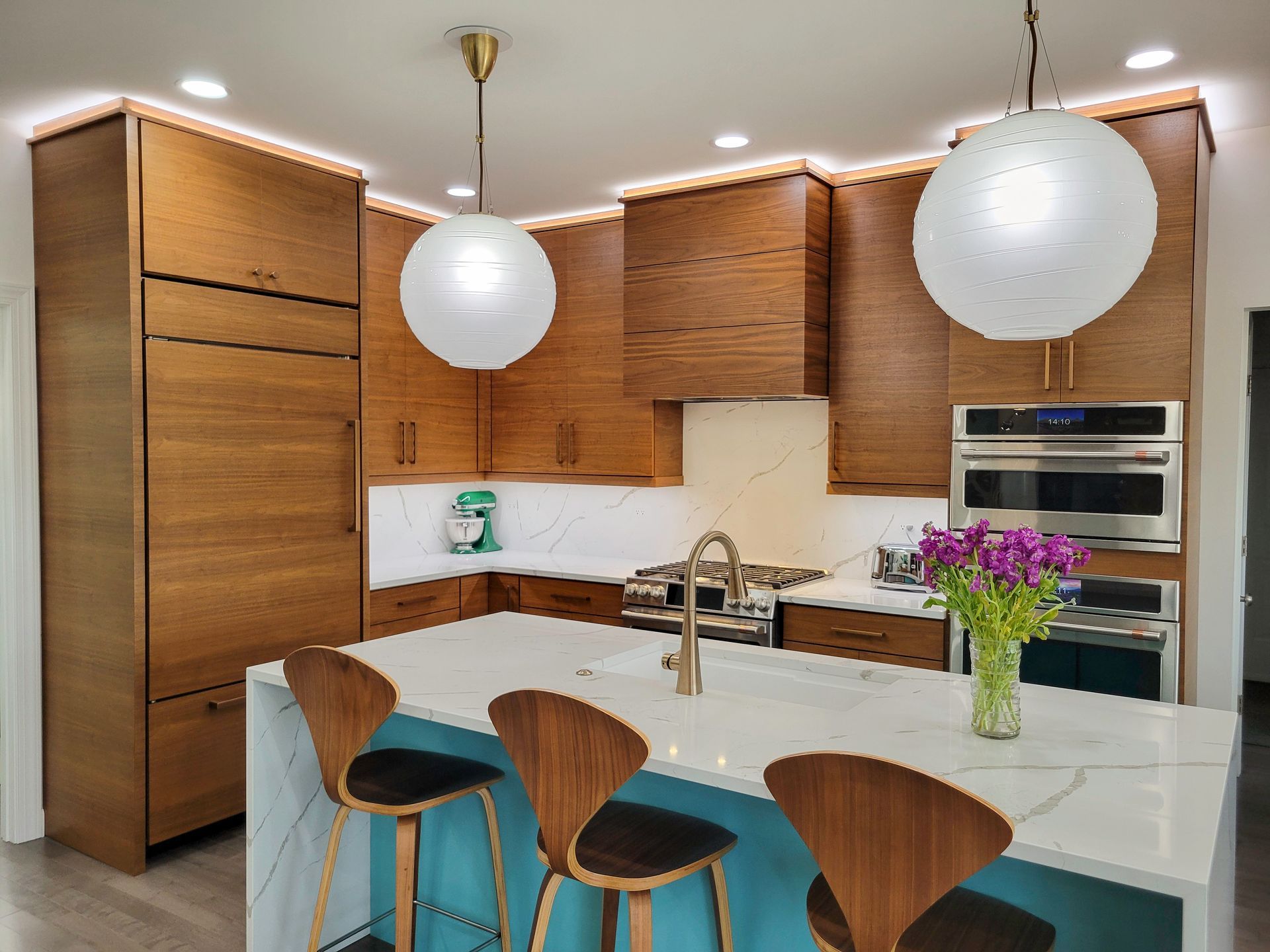 Modern kitchen with wood cabinets, white island, round pendant lights, and turquoise stools