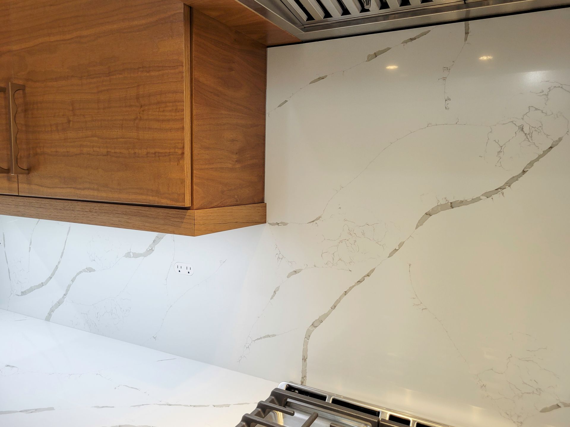 Kitchen corner with white marble-look backsplash, wood cabinets, and a stovetop below.