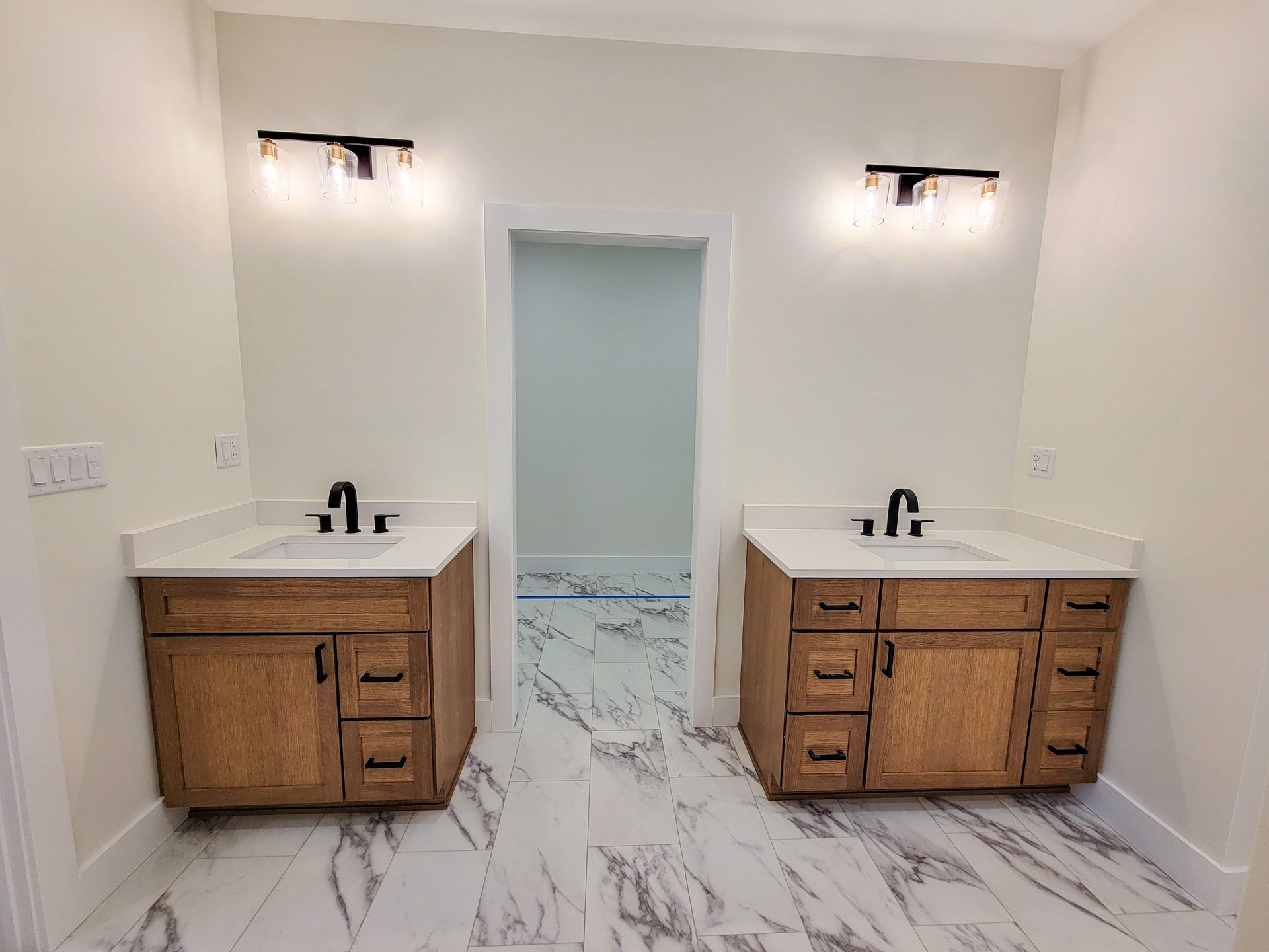 Modern bathroom with two wooden vanities, white sinks, marble floor, and a doorway to a shower area