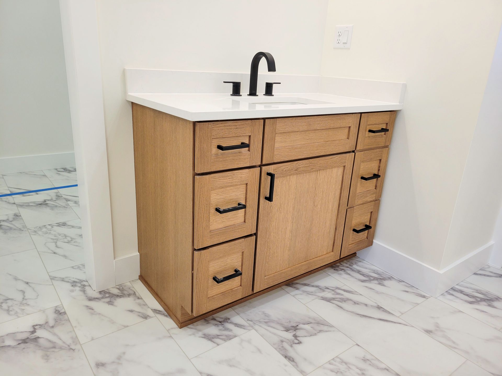 Modern bathroom vanity with wood cabinets, white countertop, and black faucet on marble floor