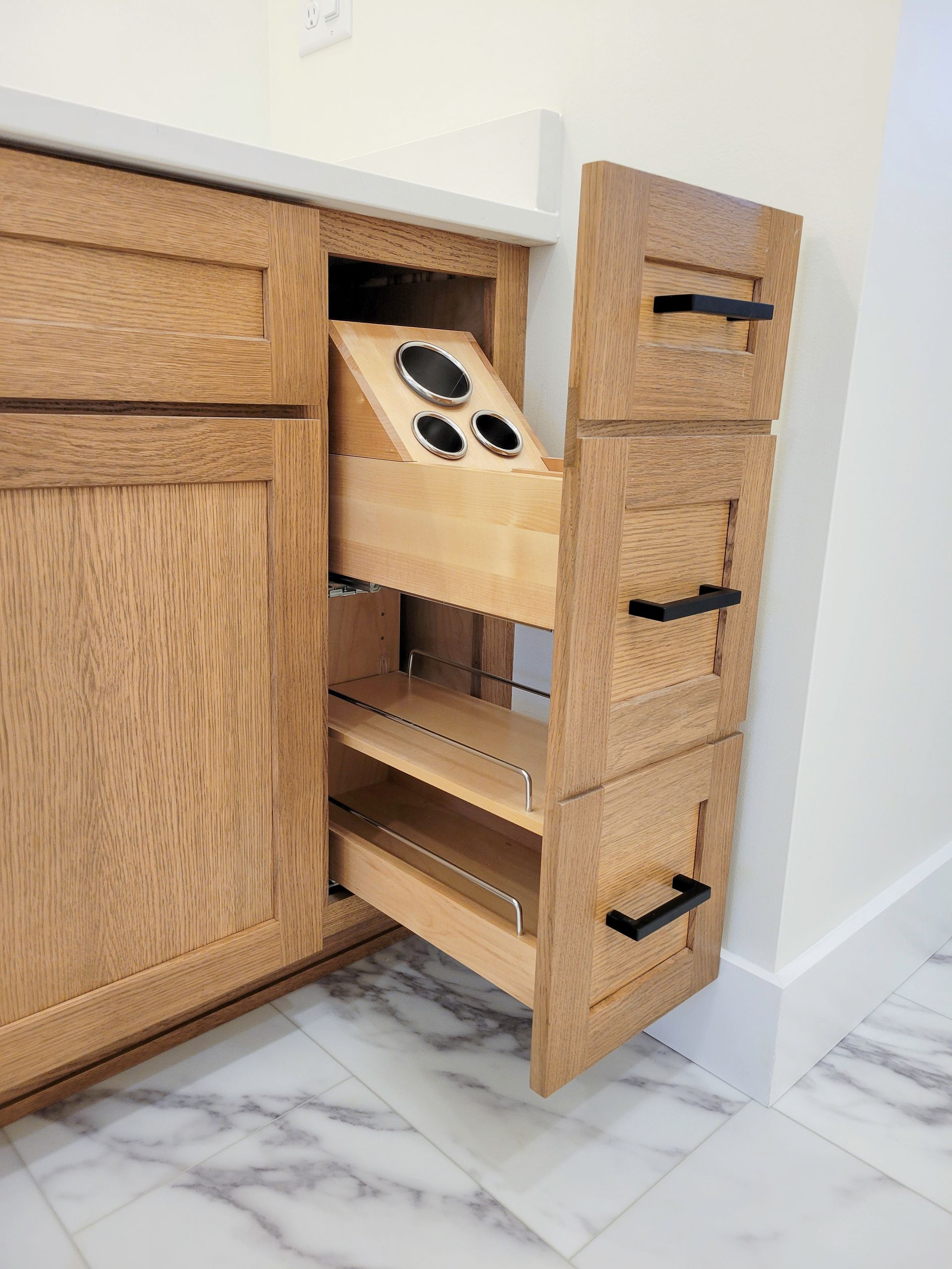 Open kitchen drawer organizer with woven baskets and black handles beside a cabinet.