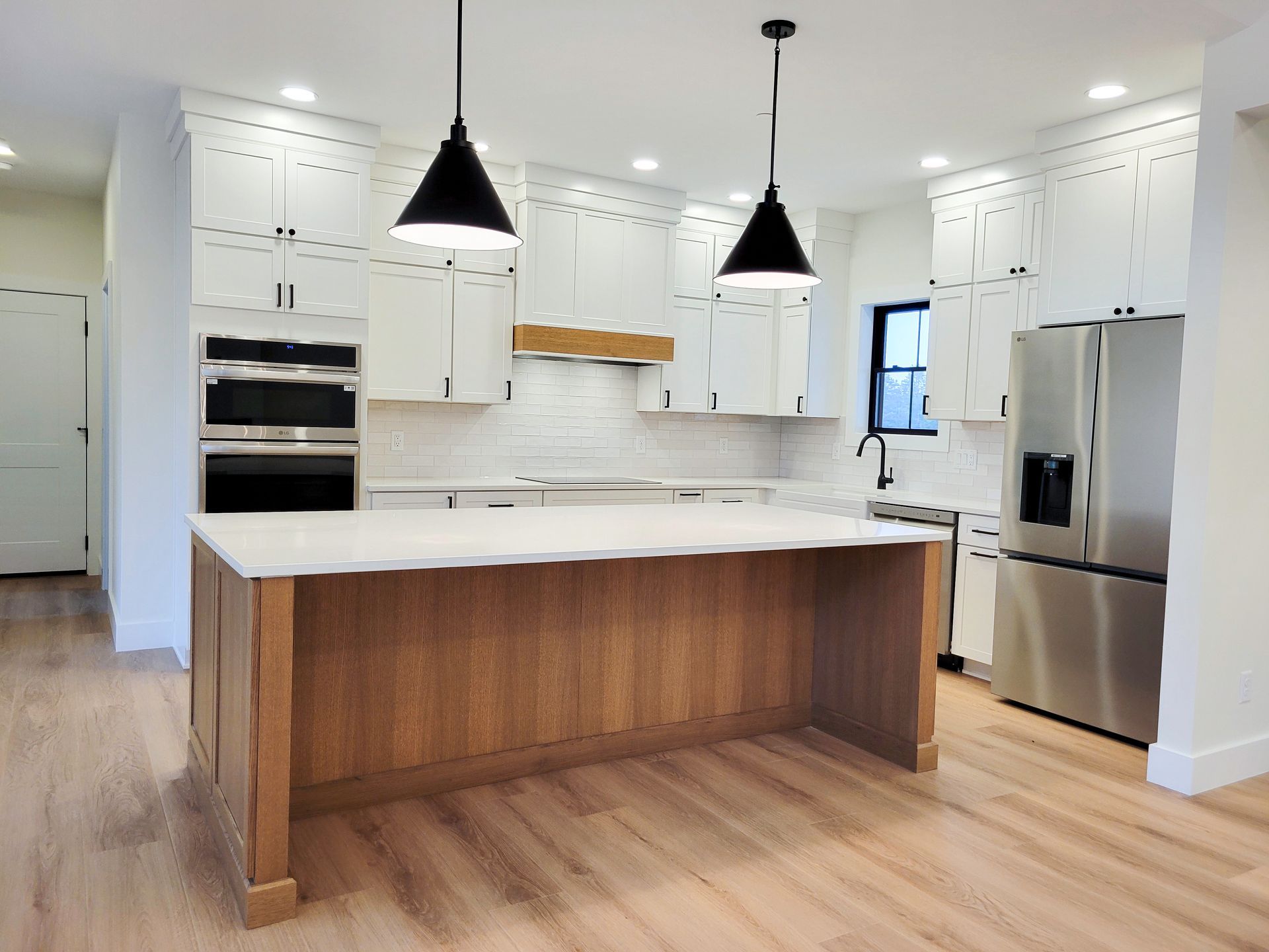Bright white modern kitchen with a wood island, black pendant lights, stainless appliances, and a large window.