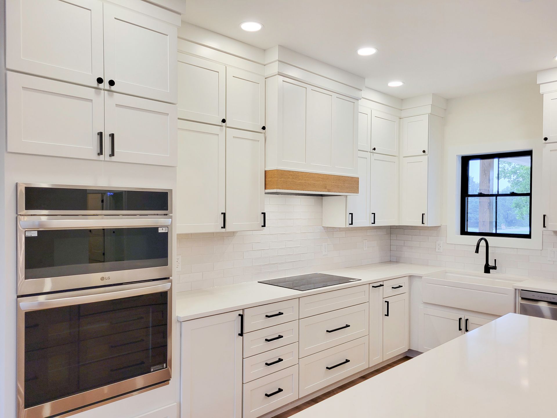Bright white modern kitchen with built-in ovens, black hardware, marble counters, and a window over the sink