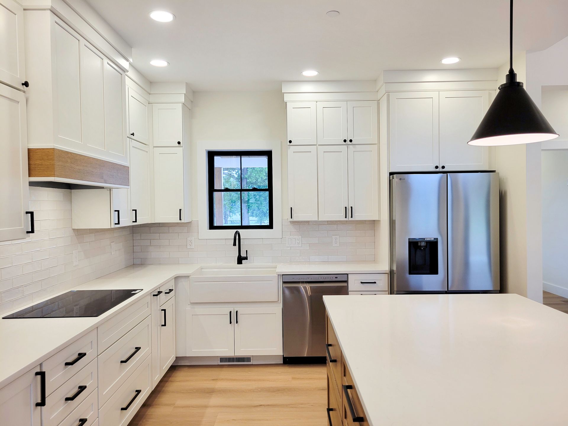 Bright white modern kitchen with island, stainless steel fridge, and black pendant light