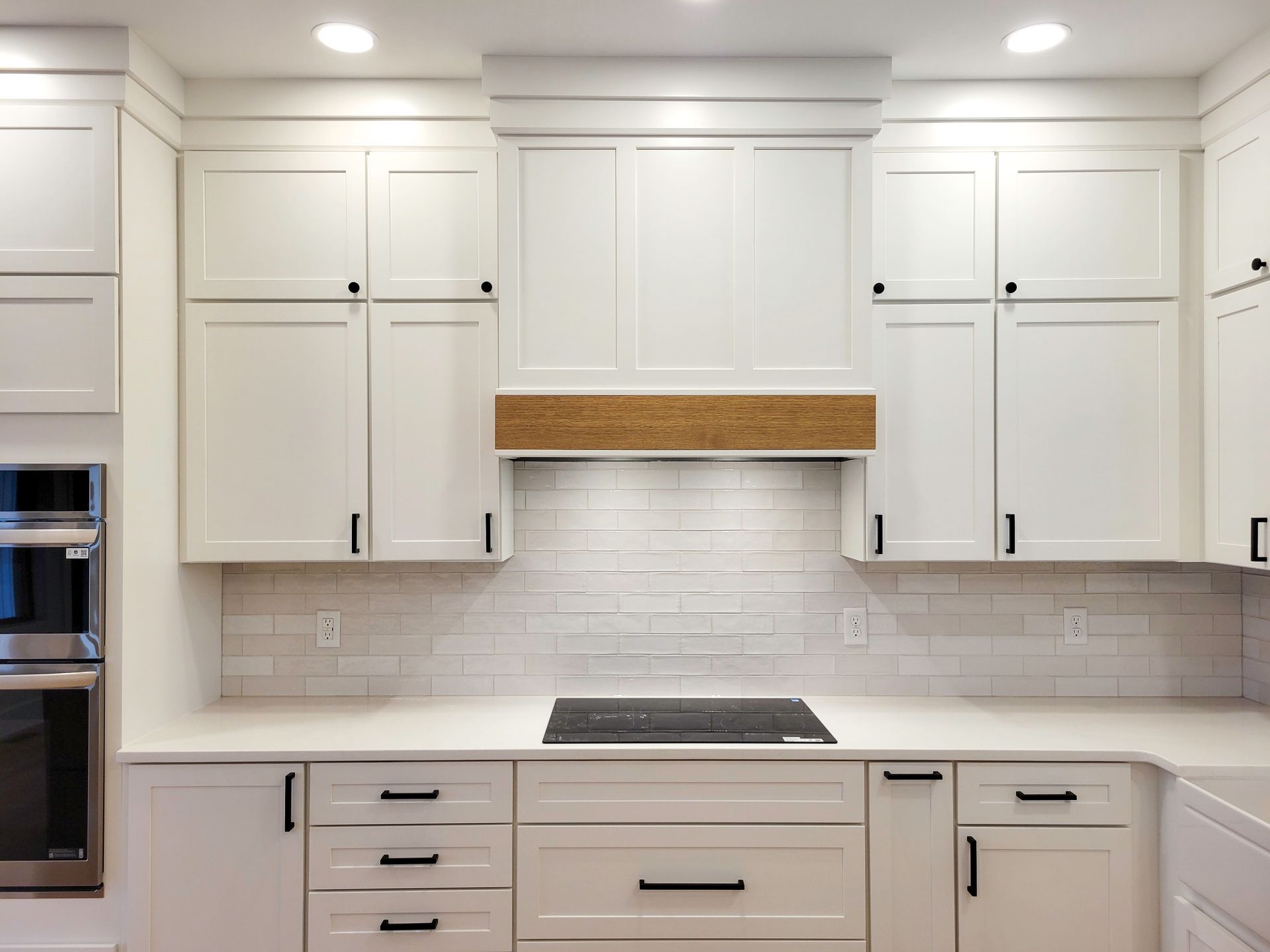Modern white kitchen with cabinets, subway tile backsplash, and a wooden range hood accent