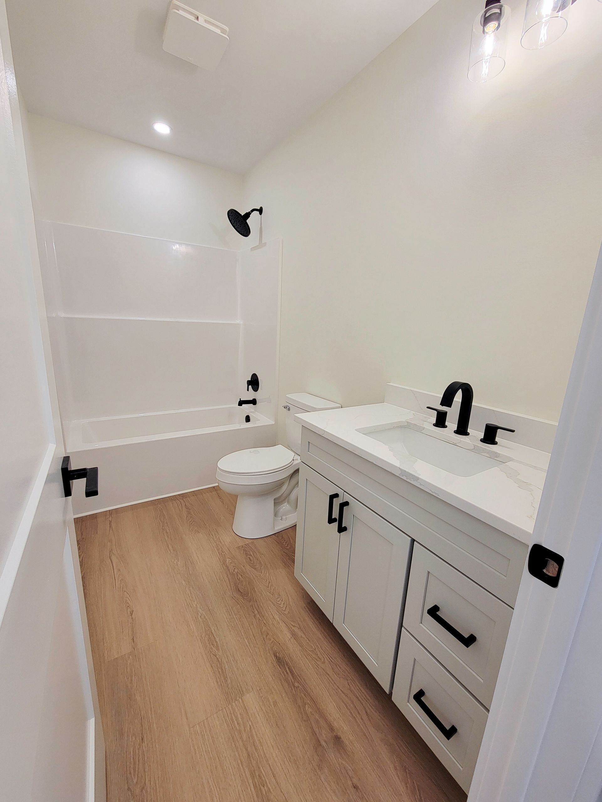 Narrow white bathroom with wood-look floor, vanity, toilet, and shower/tub alcove.