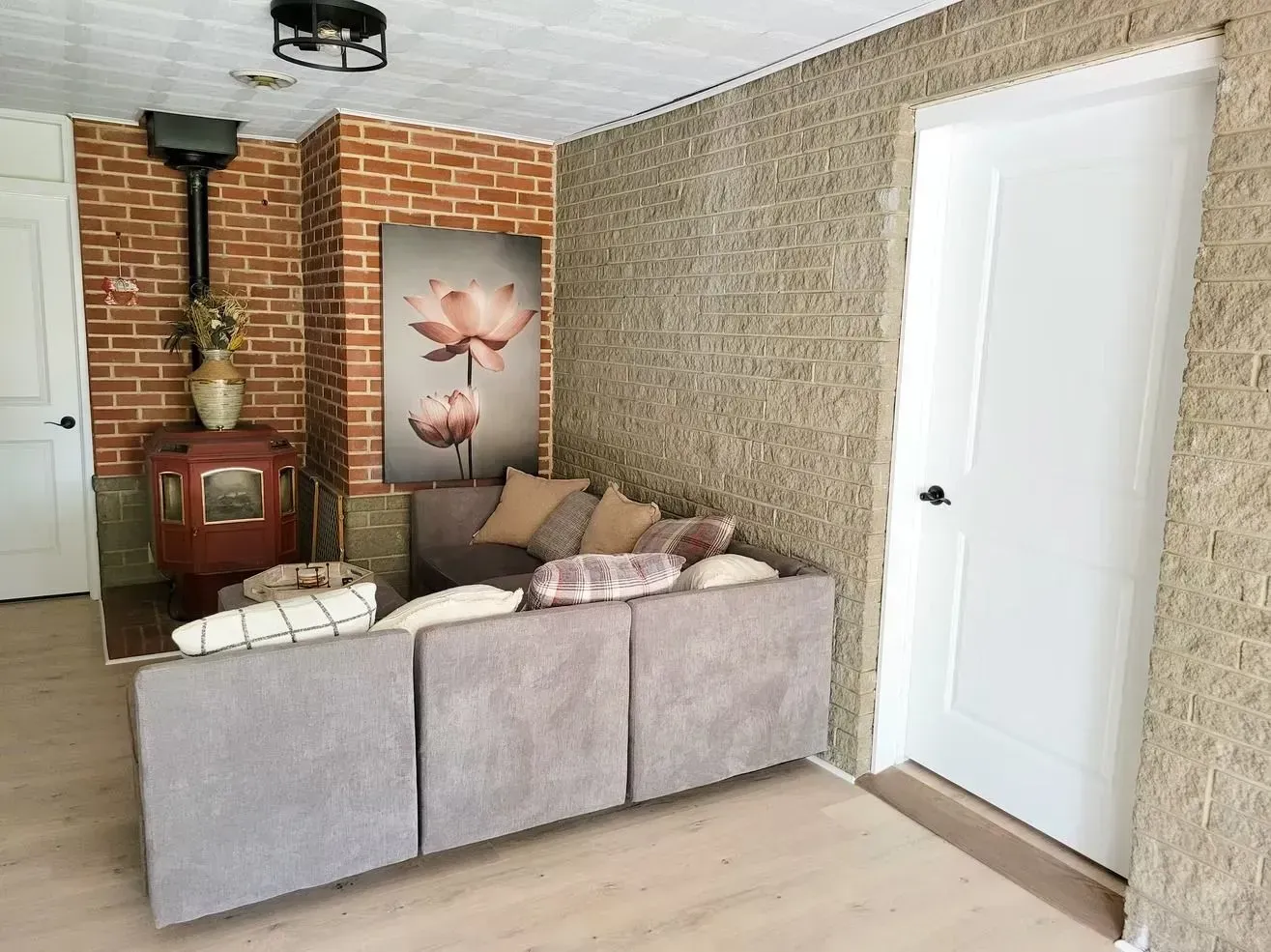 Living room with brick wall, sofa, wood-burning stove, large flower art, and white door.