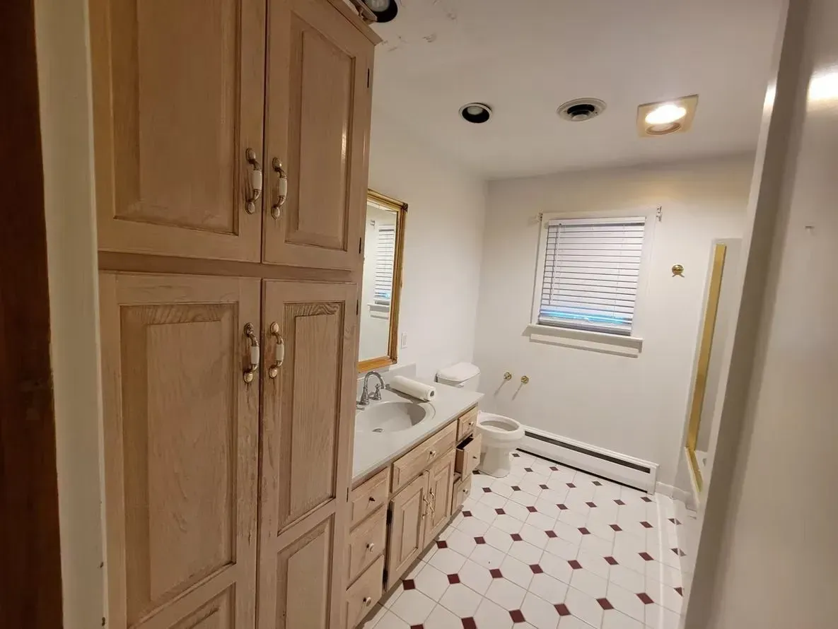 Bathroom with light wood cabinets, white walls, and a patterned floor.