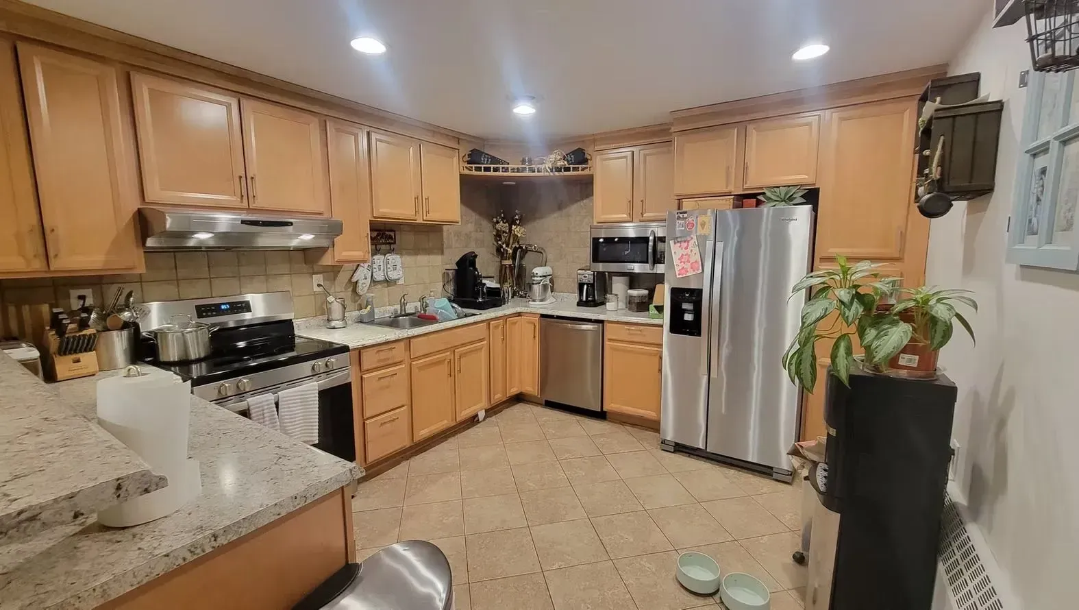 Kitchen with light wood cabinets, stainless steel appliances, and beige tile floor.