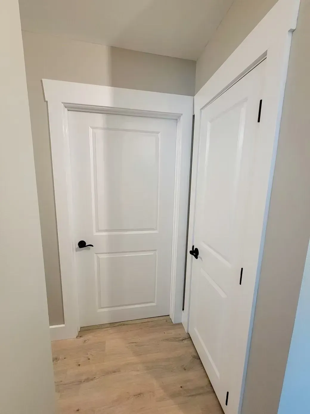 Two white doors with black handles in a hallway with light wood-look flooring.