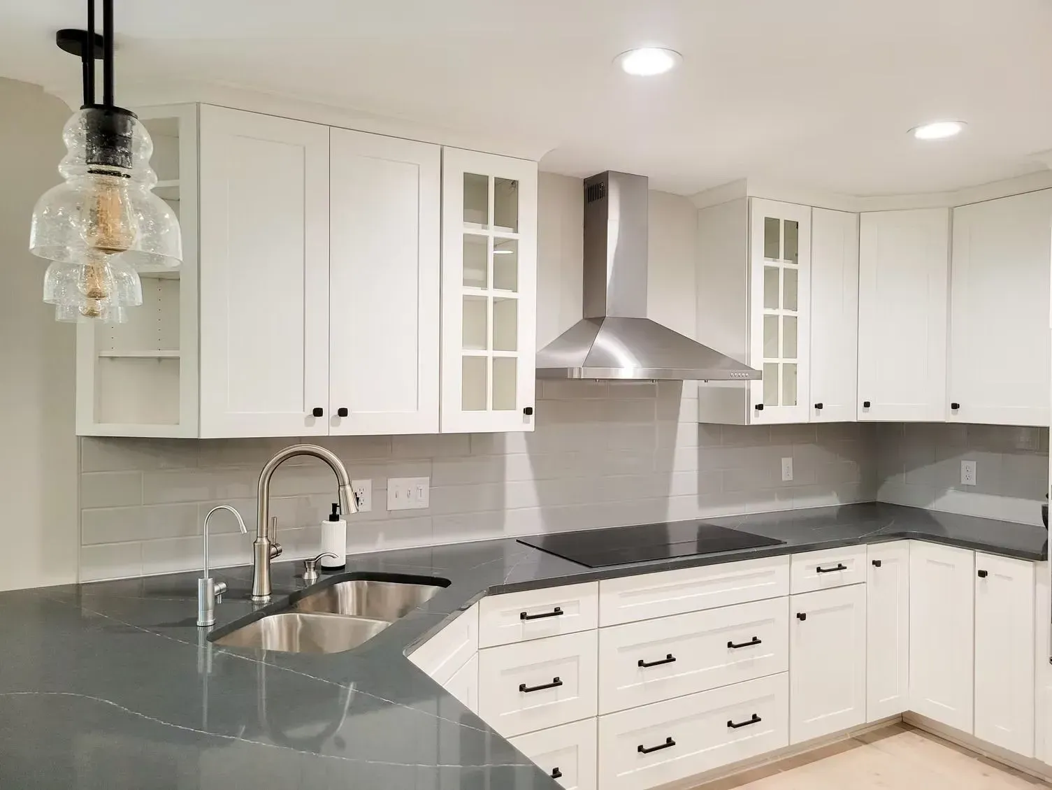 Modern white kitchen with gray countertops, stainless steel range hood, and pendant light fixture.