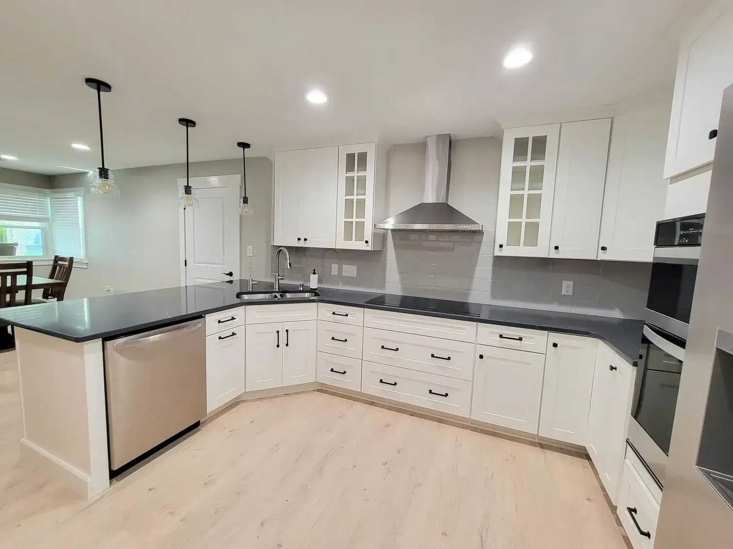 Modern white kitchen with stainless steel appliances, dark countertops, and light wood flooring.