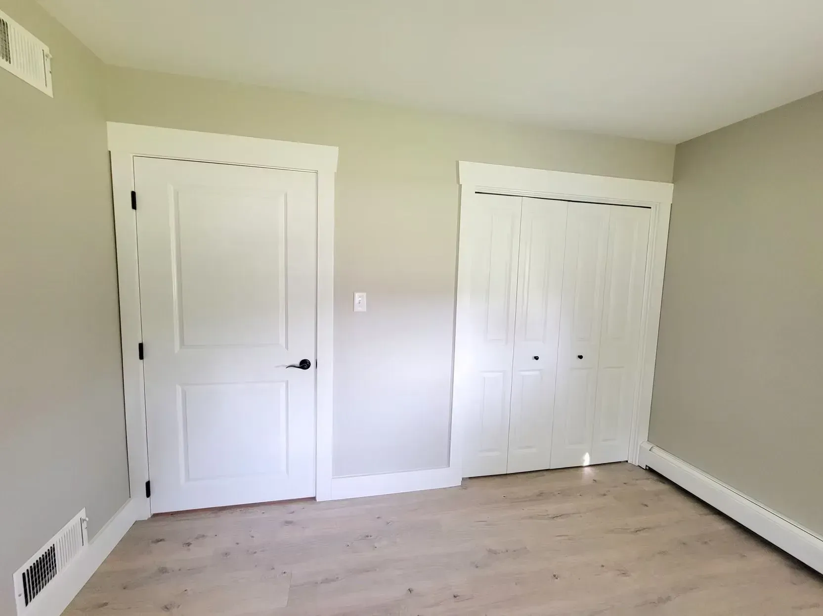 Empty bedroom with a white door and closet, light wood-look floors, and tan walls.
