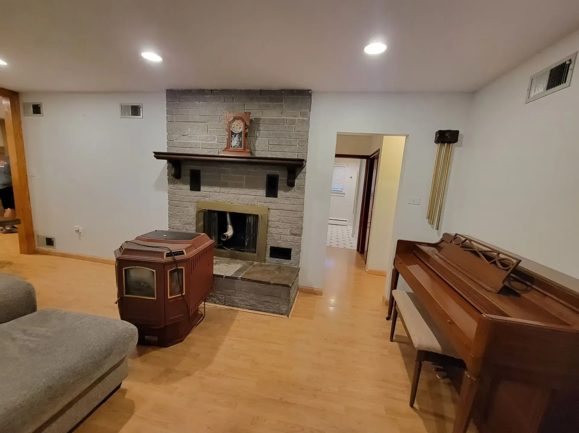 Living room with a fireplace, piano, wood stove, and light wood flooring.