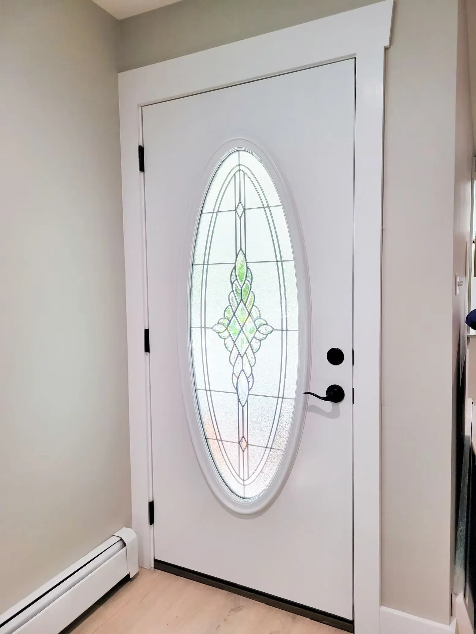 White front door with oval glass panel and decorative details, black handle and hinges, inside a home.
