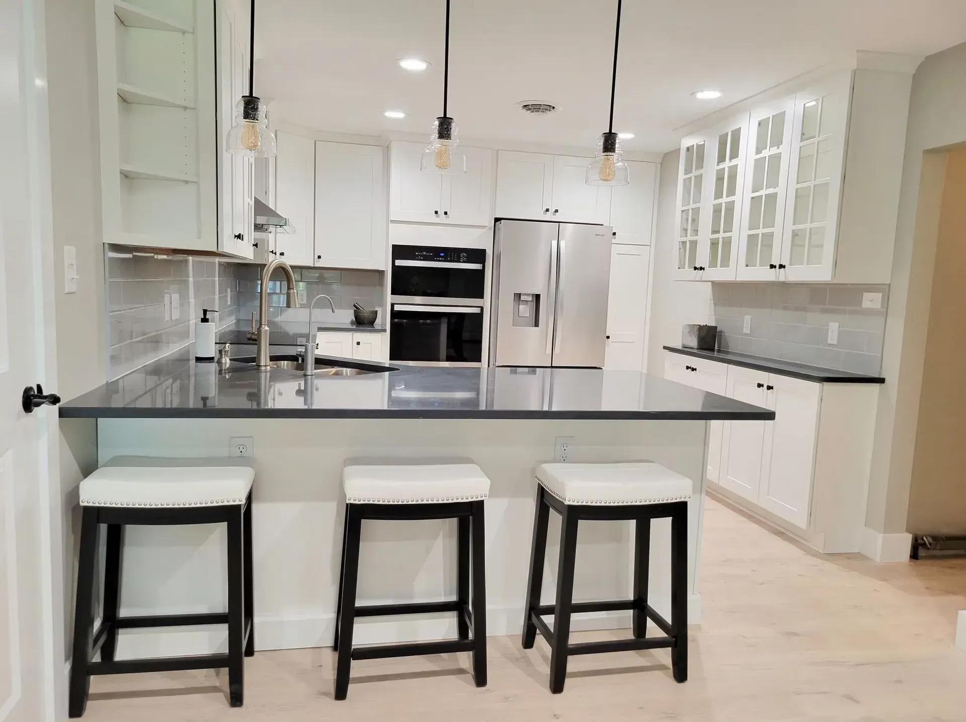 Modern kitchen with white cabinets, dark countertops, and three stools at the island.