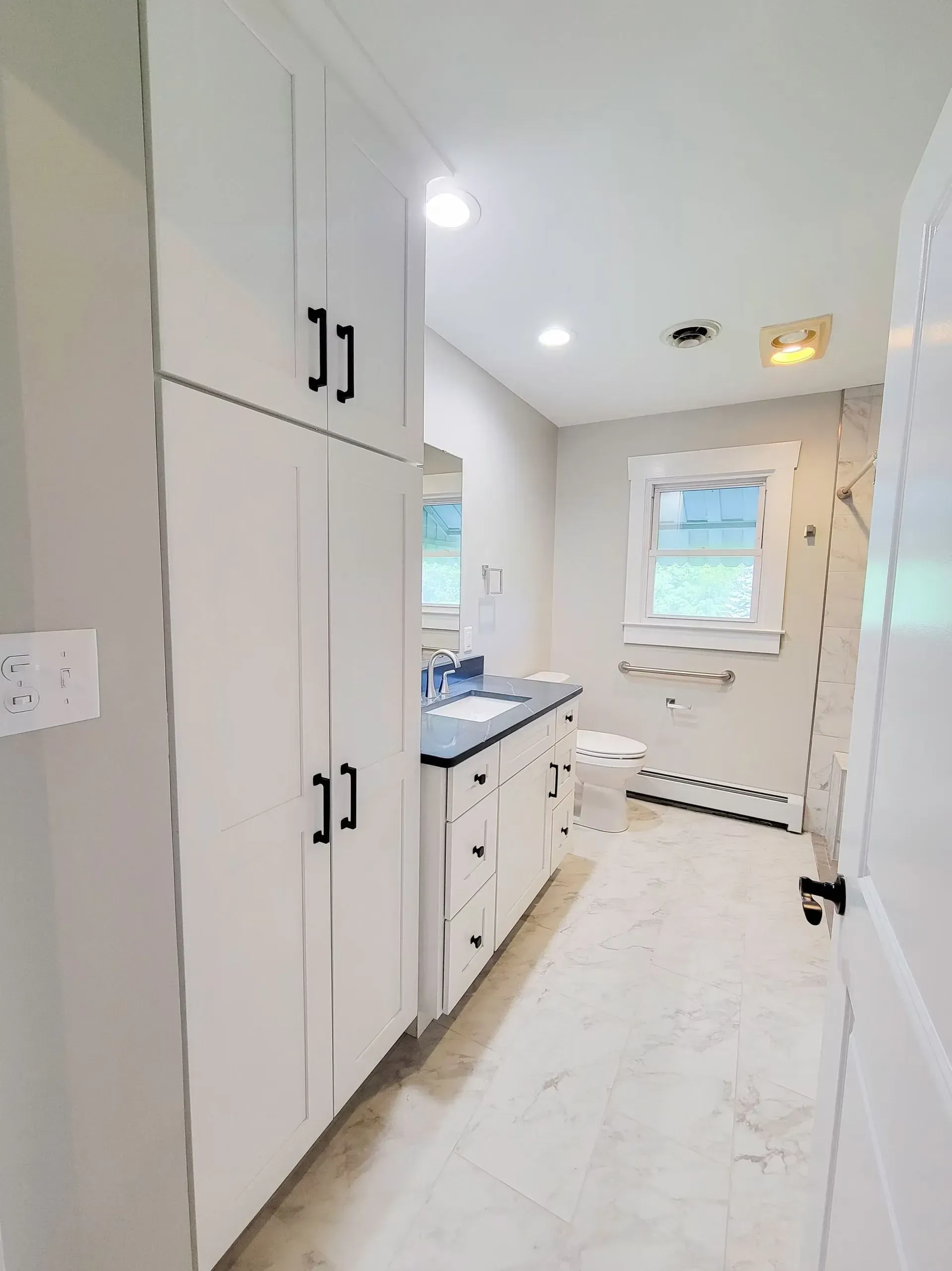 White bathroom with tall storage cabinets, vanity, and window.