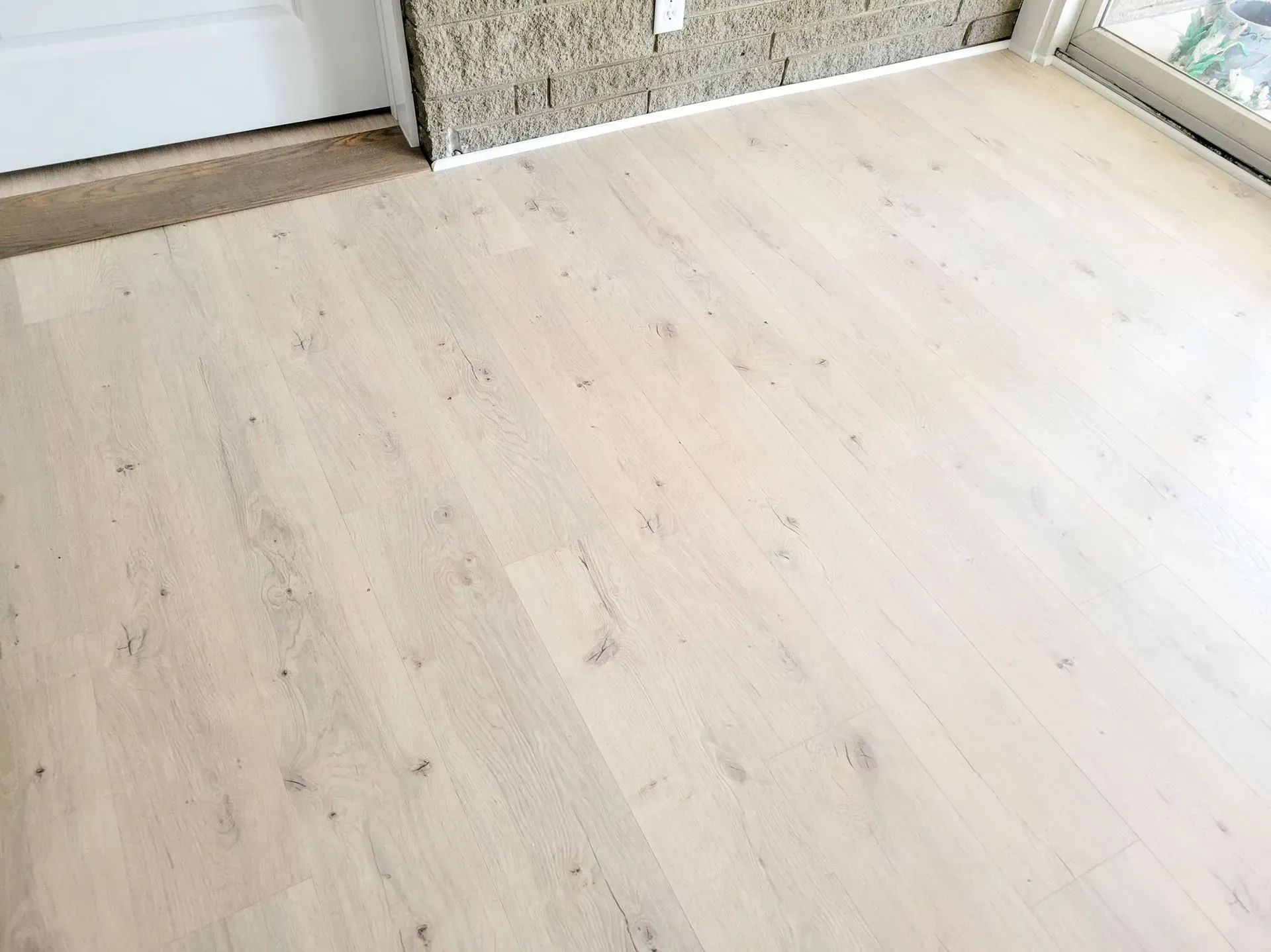 Light wood flooring in a room next to a white door and textured wall.