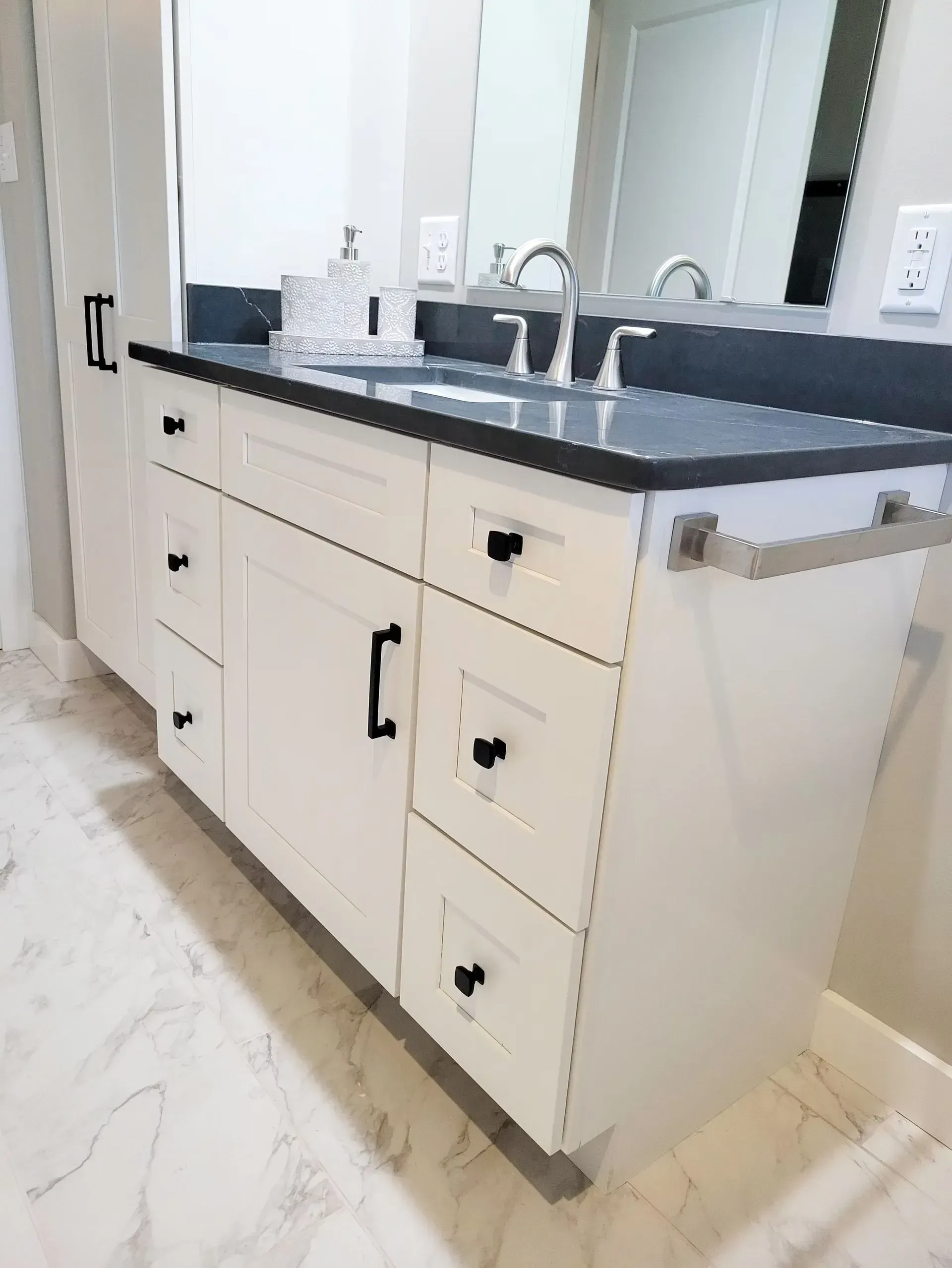 White bathroom vanity with black countertop and hardware. Silver fixtures and towel bar.