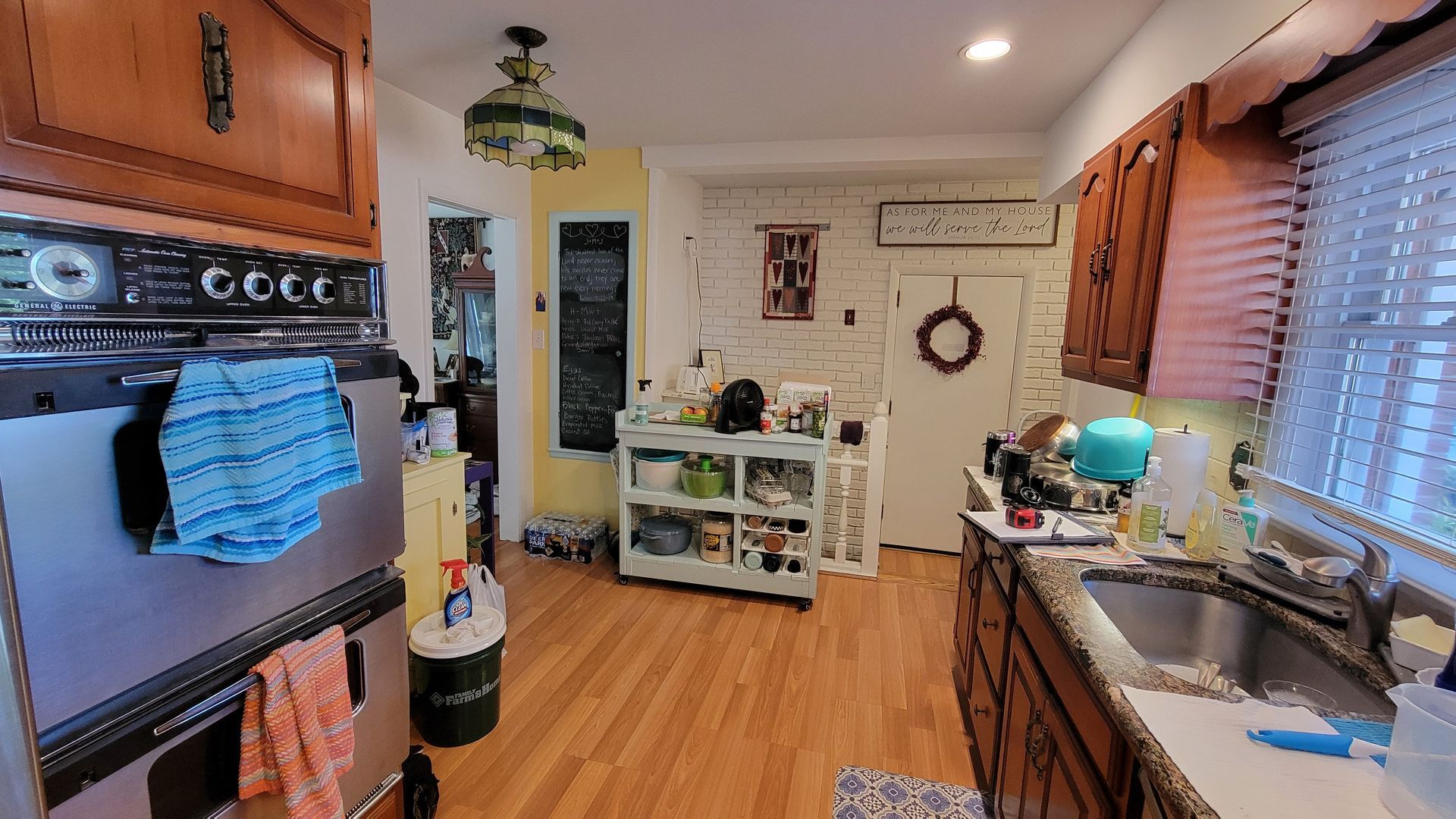 Kitchen interior with wooden cabinets, a stainless steel oven, a sink, and a white brick wall.