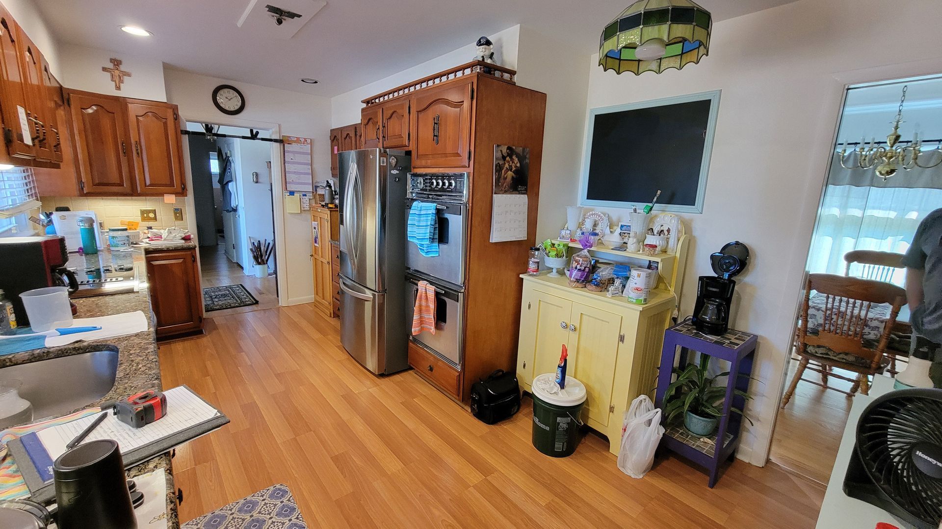 Kitchen with wooden cabinets, stainless steel refrigerator, and yellow hutch, featuring wood-look flooring and multiple doorways.