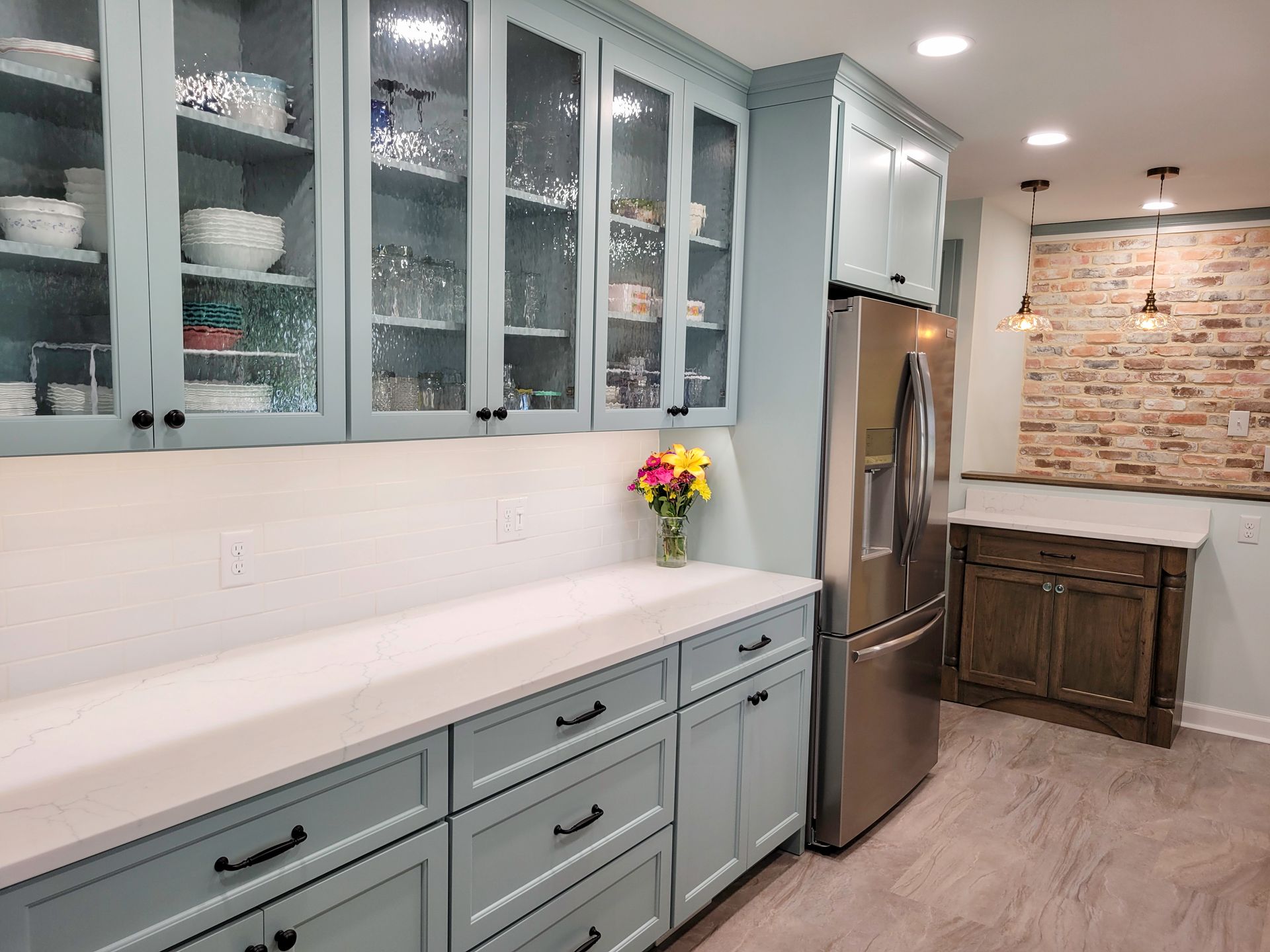 Kitchen with light blue cabinets, white countertops, glass-front upper cabinets, and a stainless steel refrigerator.