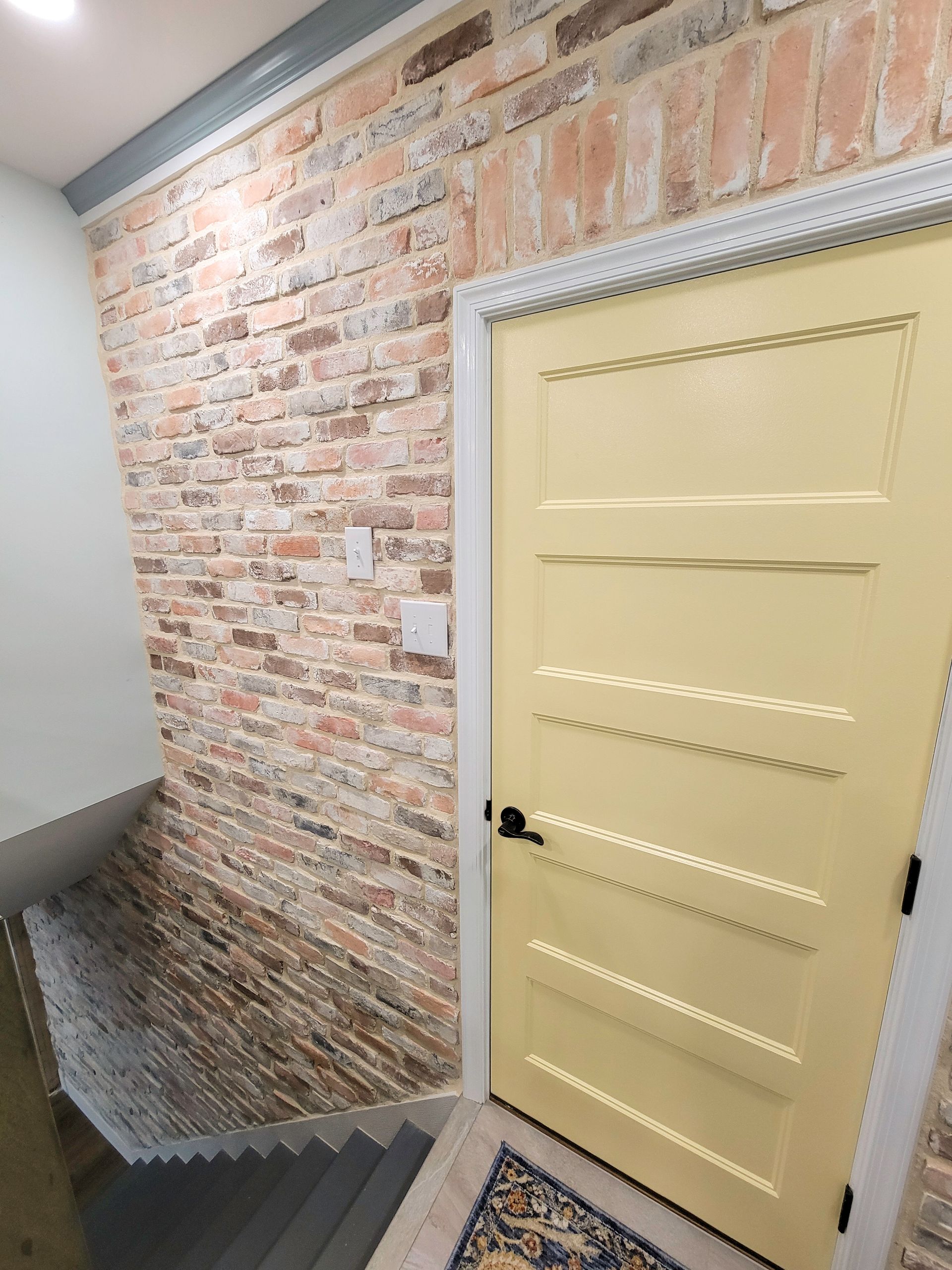 Interior with exposed brick wall, yellow door, and descending stairs.