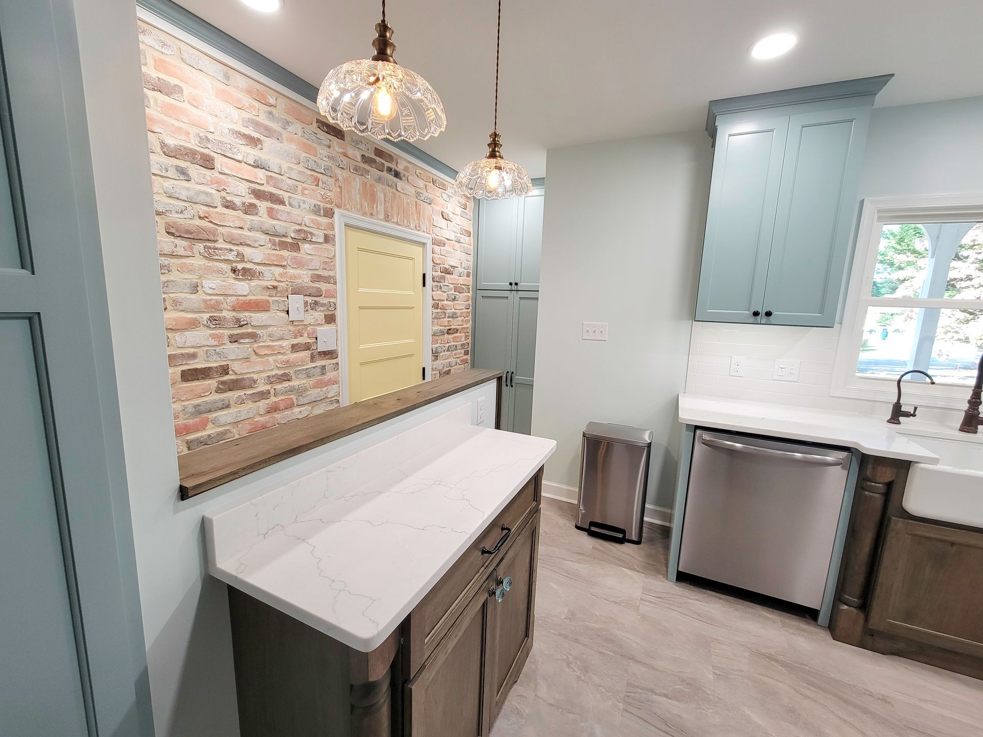 Kitchen with brick wall, blue cabinets, white countertops, and stainless steel appliances.