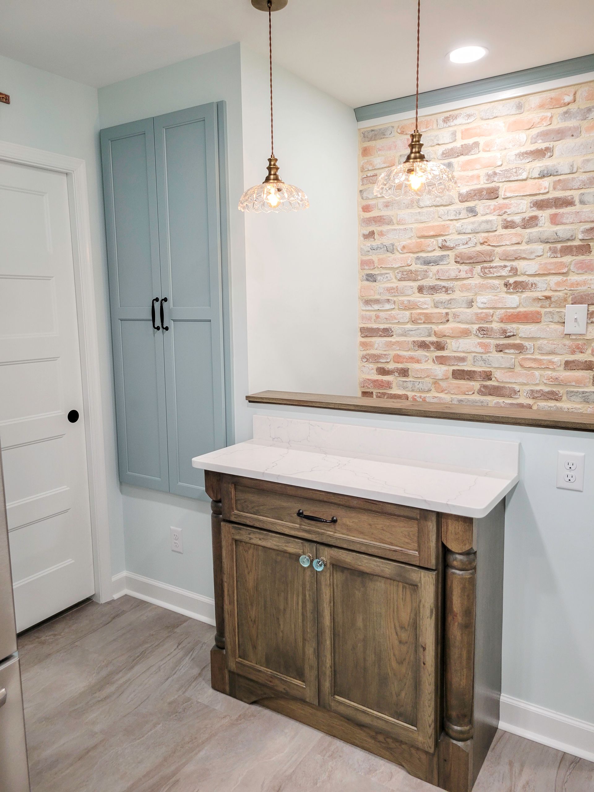 A kitchen nook with a wood cabinet, brick wall, and two pendant lights.