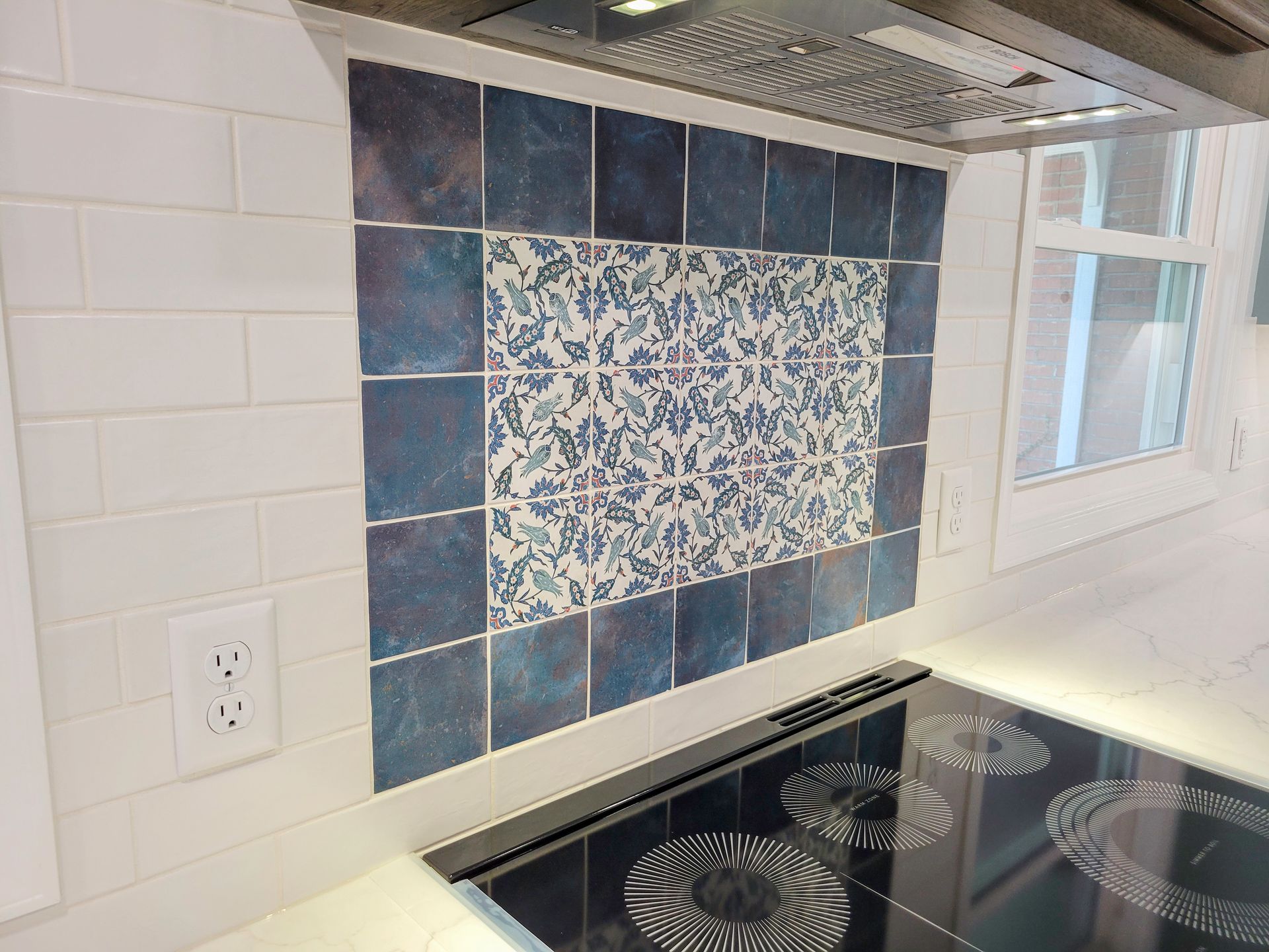 Kitchen backsplash with blue patterned tiles, bordered by solid blue tiles above a stovetop.