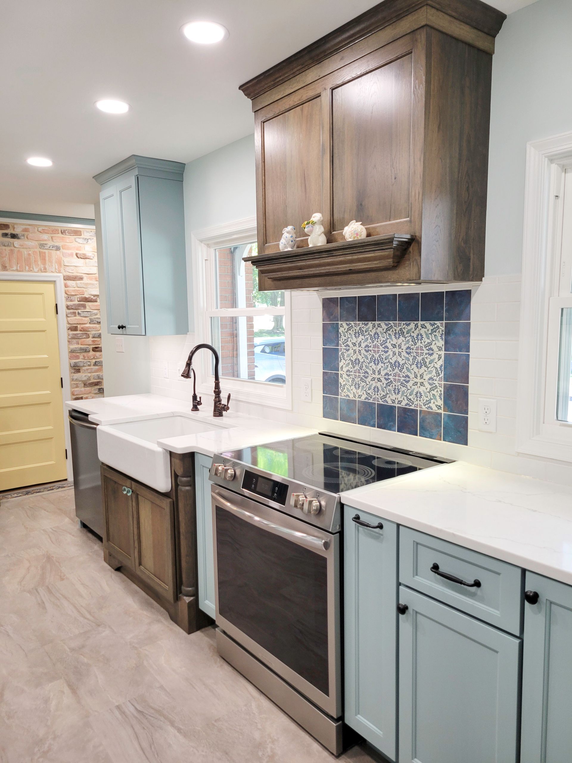 Kitchen with light blue and wood cabinets, white countertops, and brick wall.