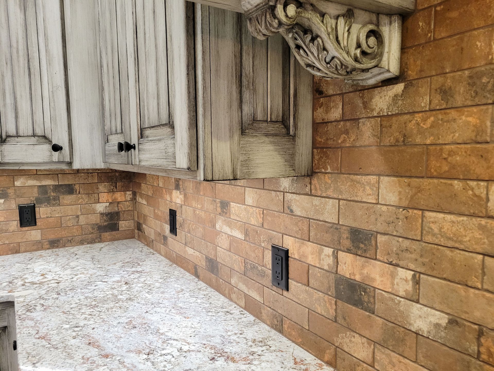 Kitchen: brick backsplash, white cabinets, decorative corbel, and speckled countertop.