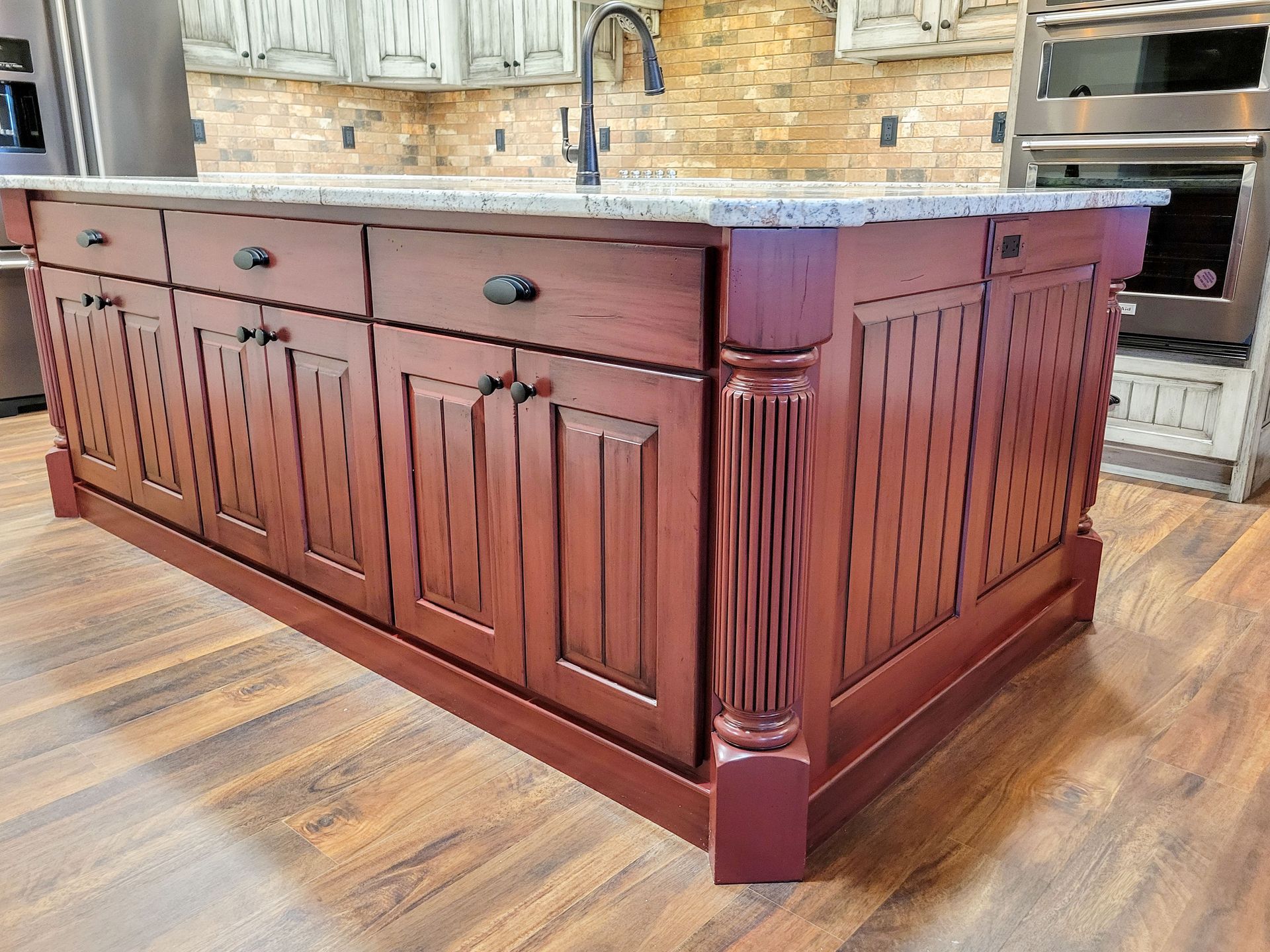 Red kitchen island with granite countertop, cabinets, and a fluted pillar.
